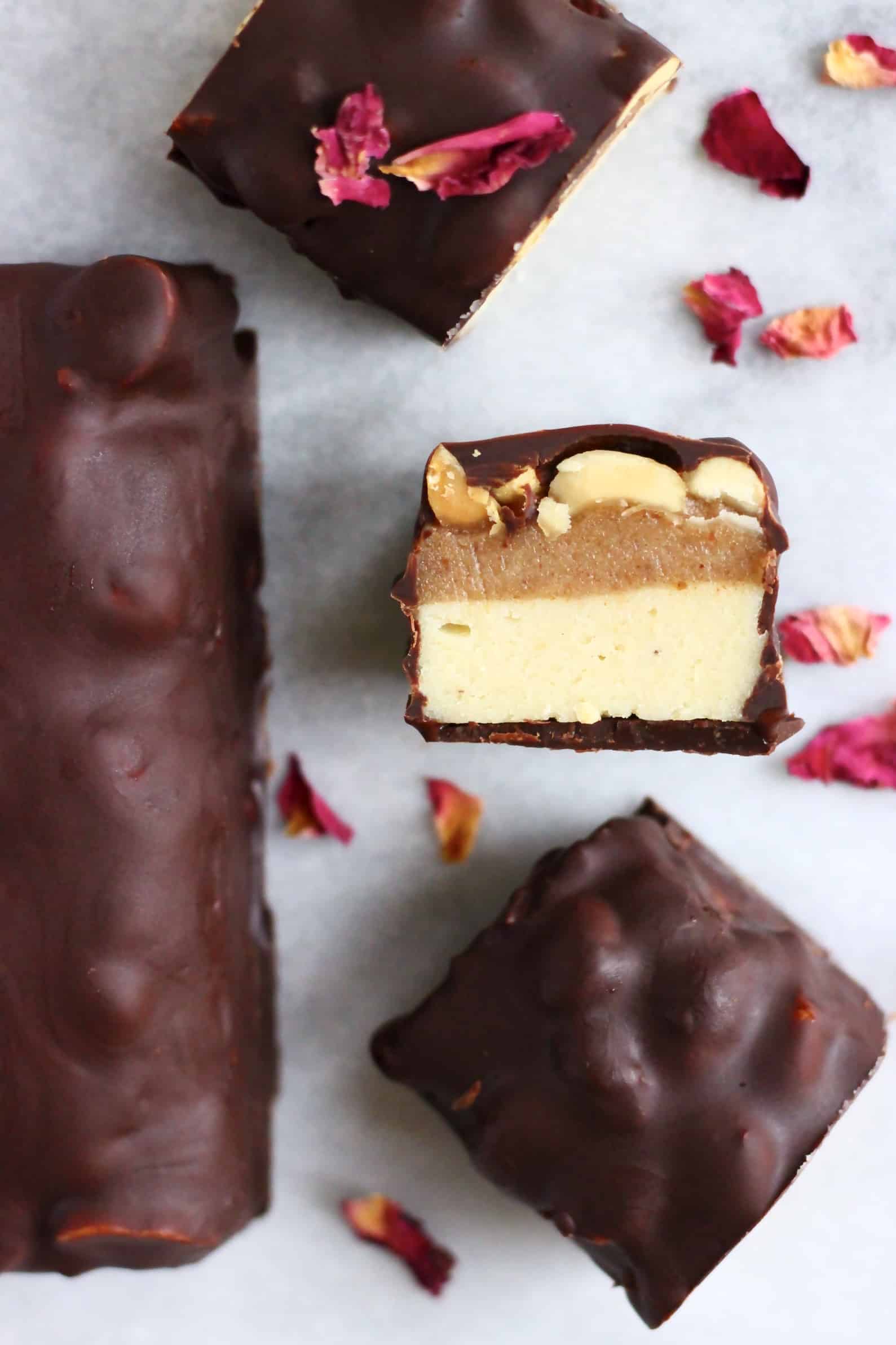 A vegan snickers bar cut into three pieces with a whole bar next to it against a piece of white paper