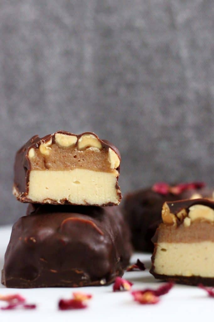 A vegan snickers bar made of nougat, caramel and peanuts cut in half on top of another bar