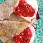 Two buckwheat crepes filled with whipped cream and jam on a green plate
