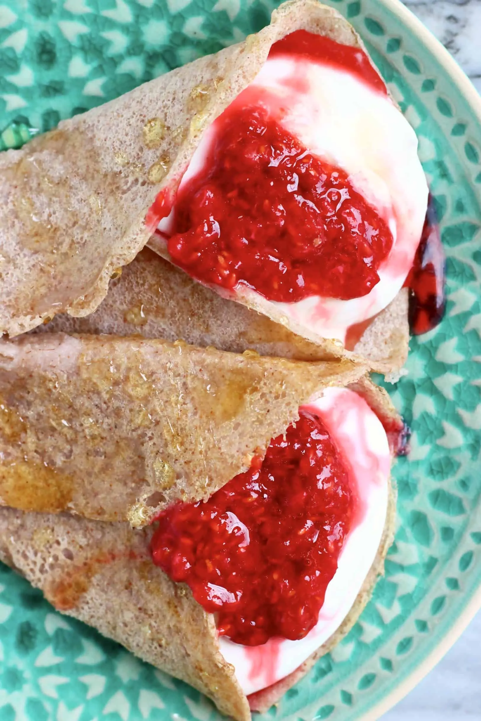 Two buckwheat crepes filled with whipped cream and jam on a green plate
