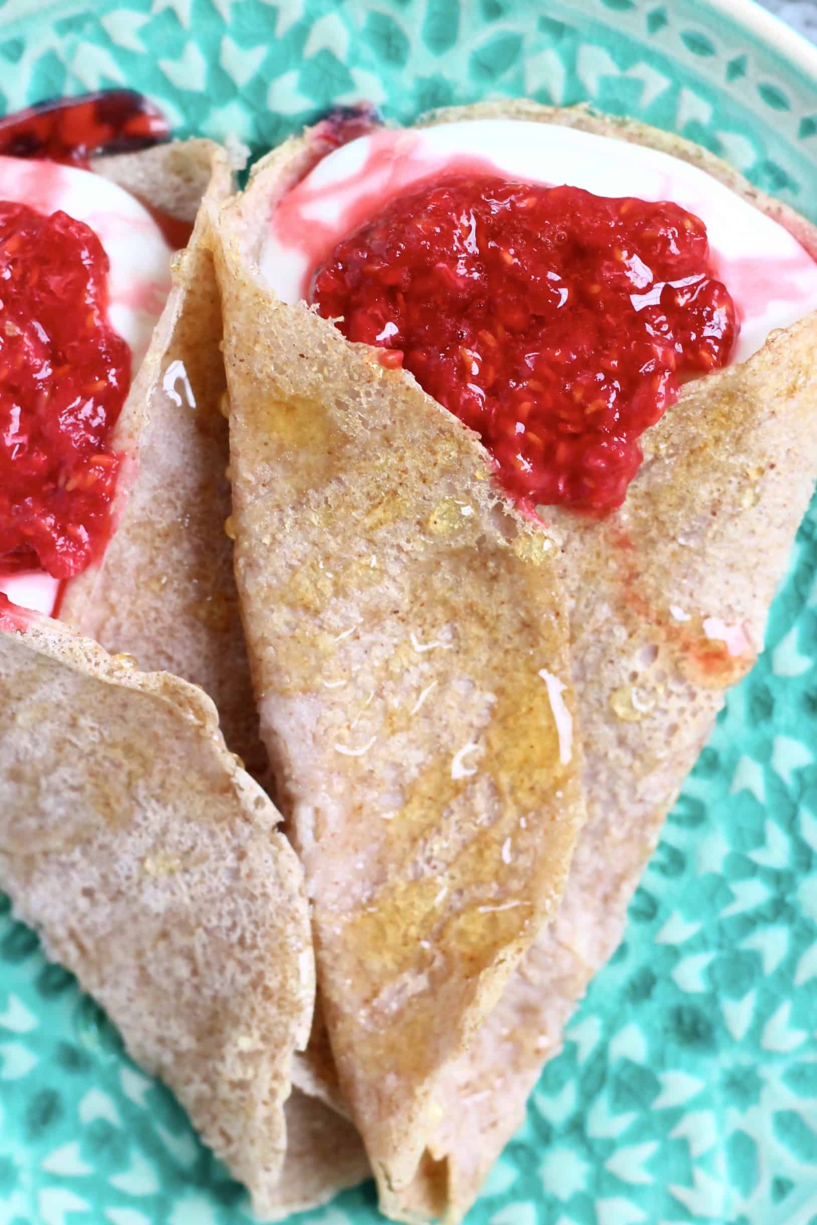 Two buckwheat crepes filled with whipped cream and jam on a green plate