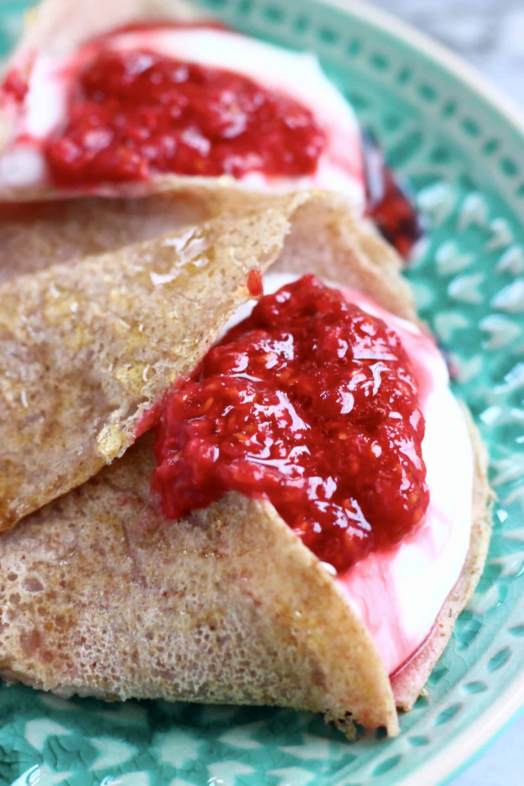 Two buckwheat crepes filled with whipped cream and jam on a green plate