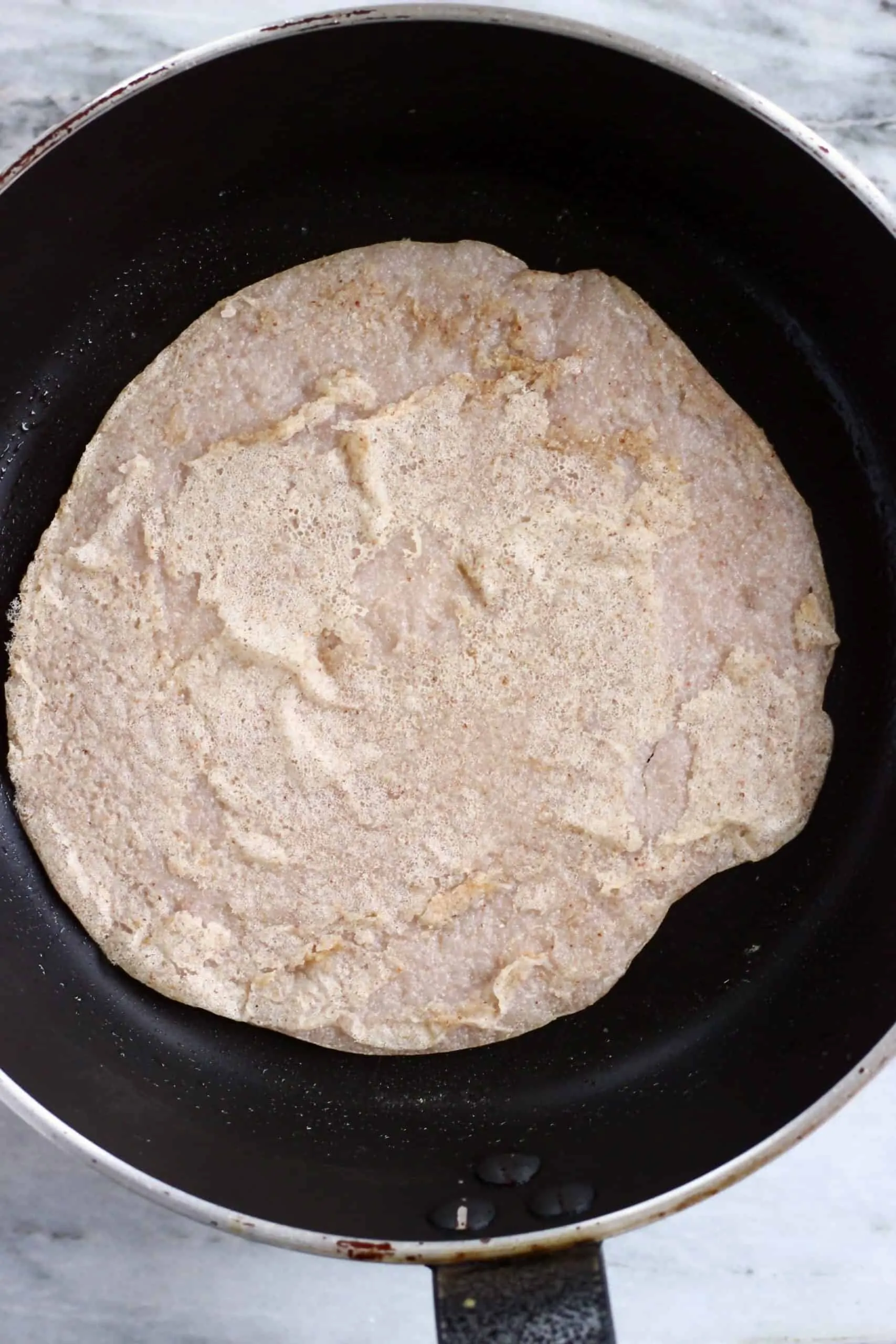A buckwheat crepe being cooked in a black frying pan