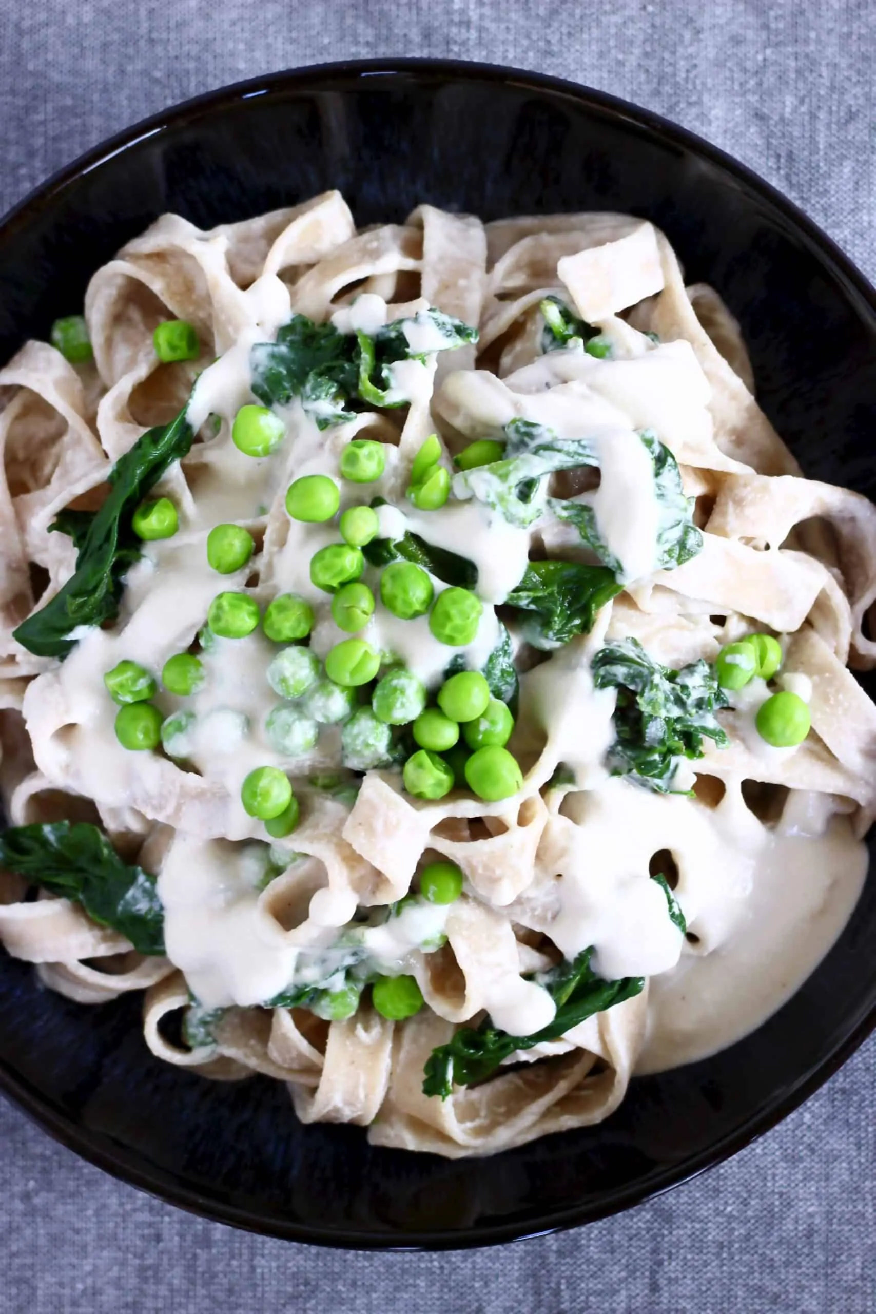 Cashew alfredo sauce pasta with green peas in a black bowl