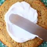 Vegan cream cheese frosting being spread over a round sponge with a palette knife on a cake stand