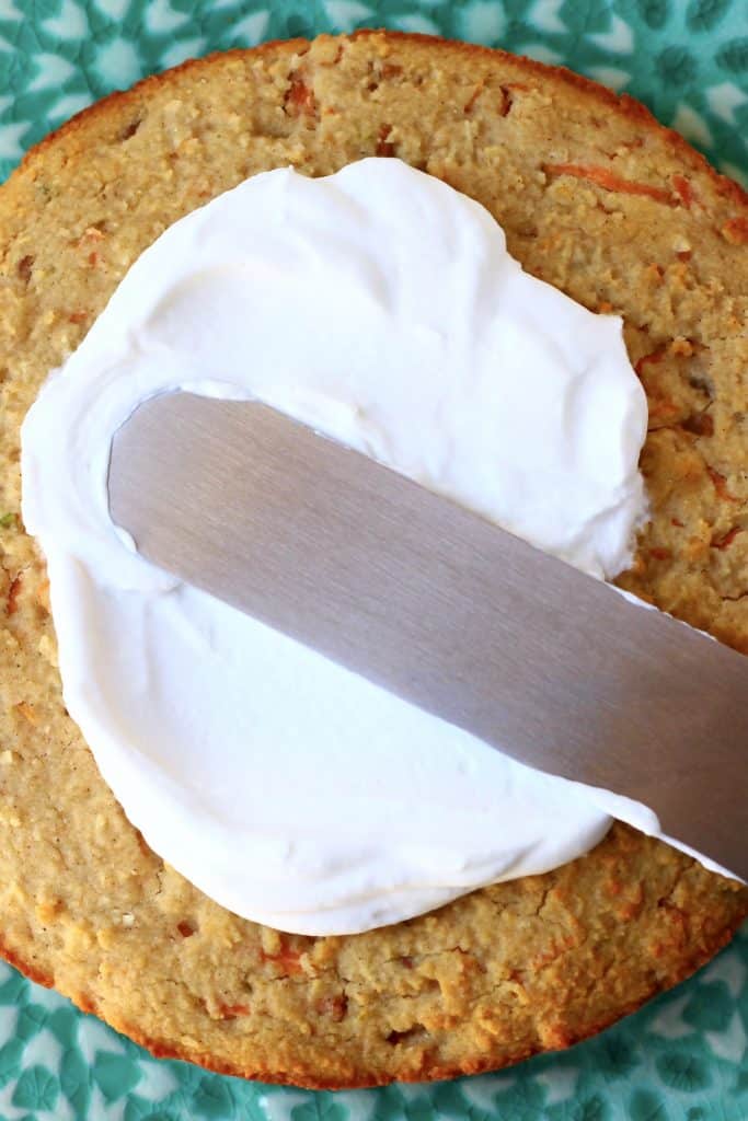 Vegan cream cheese frosting being spread over a round sponge with a palette knife on a cake stand