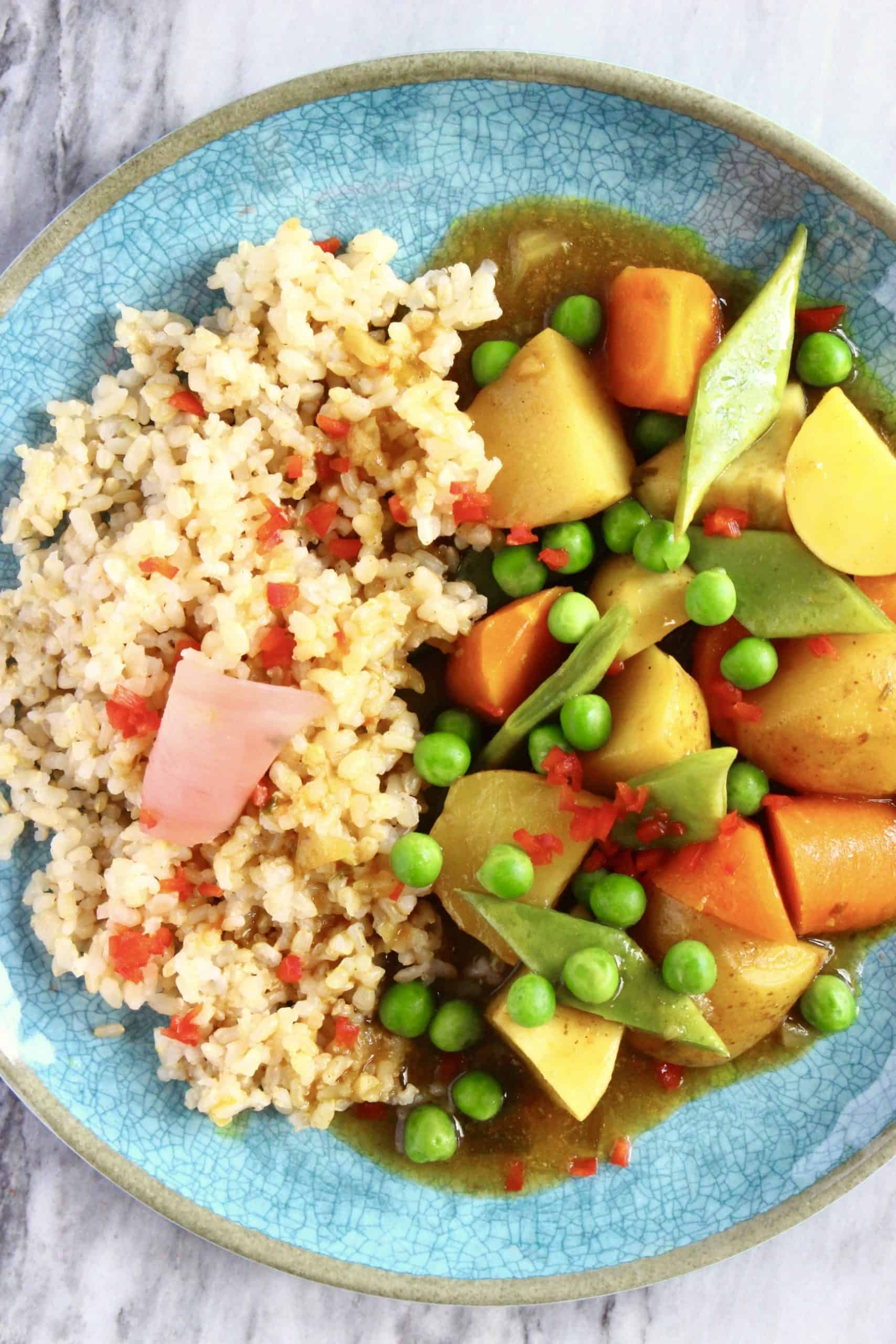 Japanese curry with potatoes, carrot and peas with brown rice on a blue plate