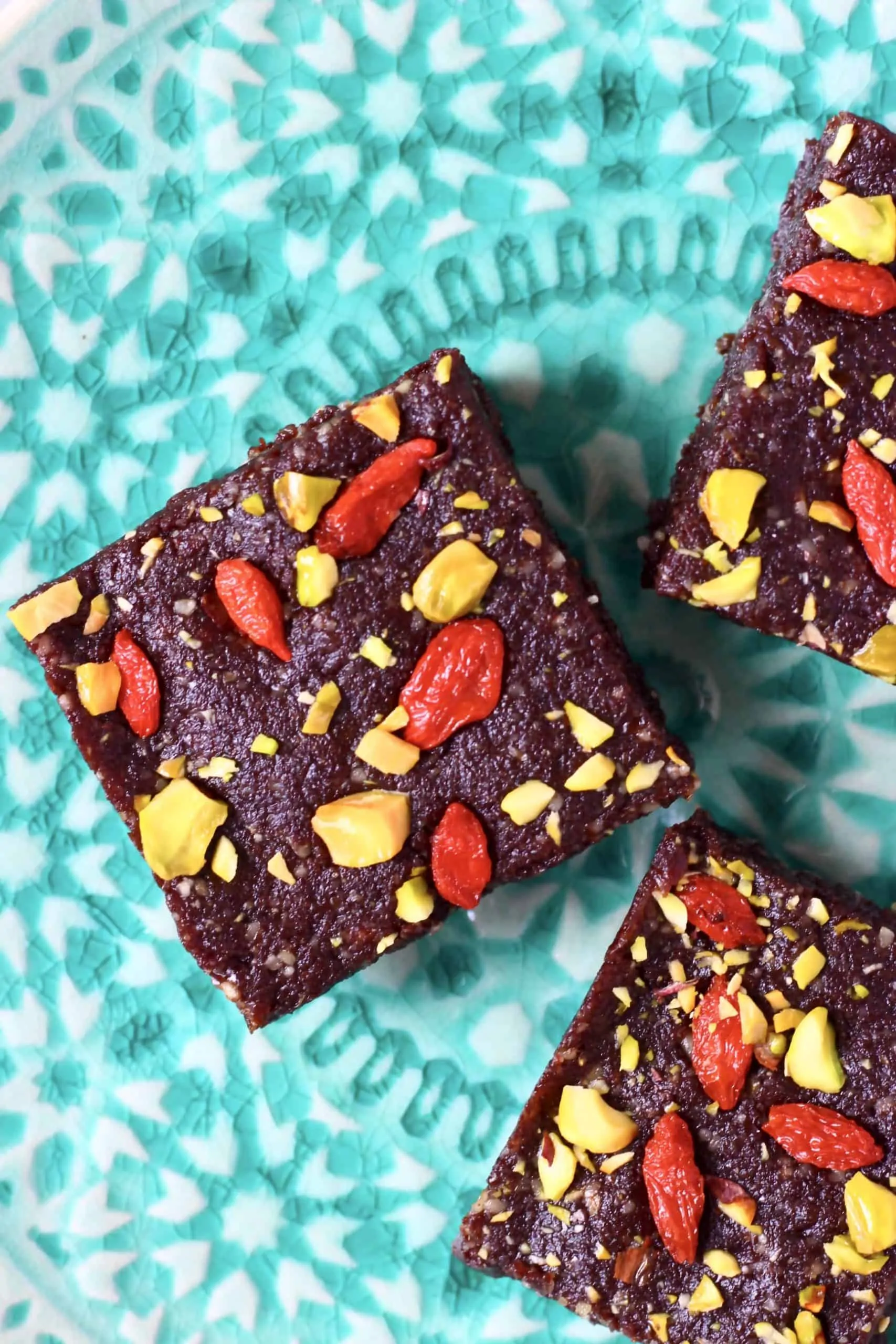 Three no-bake brownies topped with goji berries and pistachios on a green plate