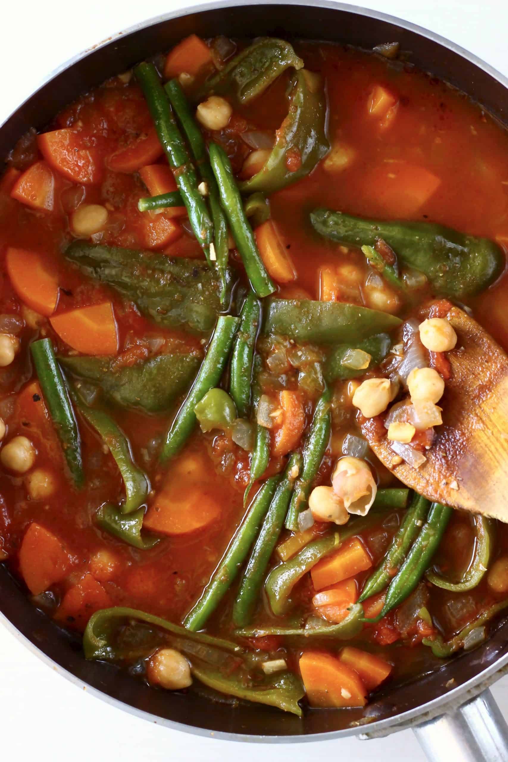 Spanish chickpea stew with vegetables in a saucepan with a wooden spatula