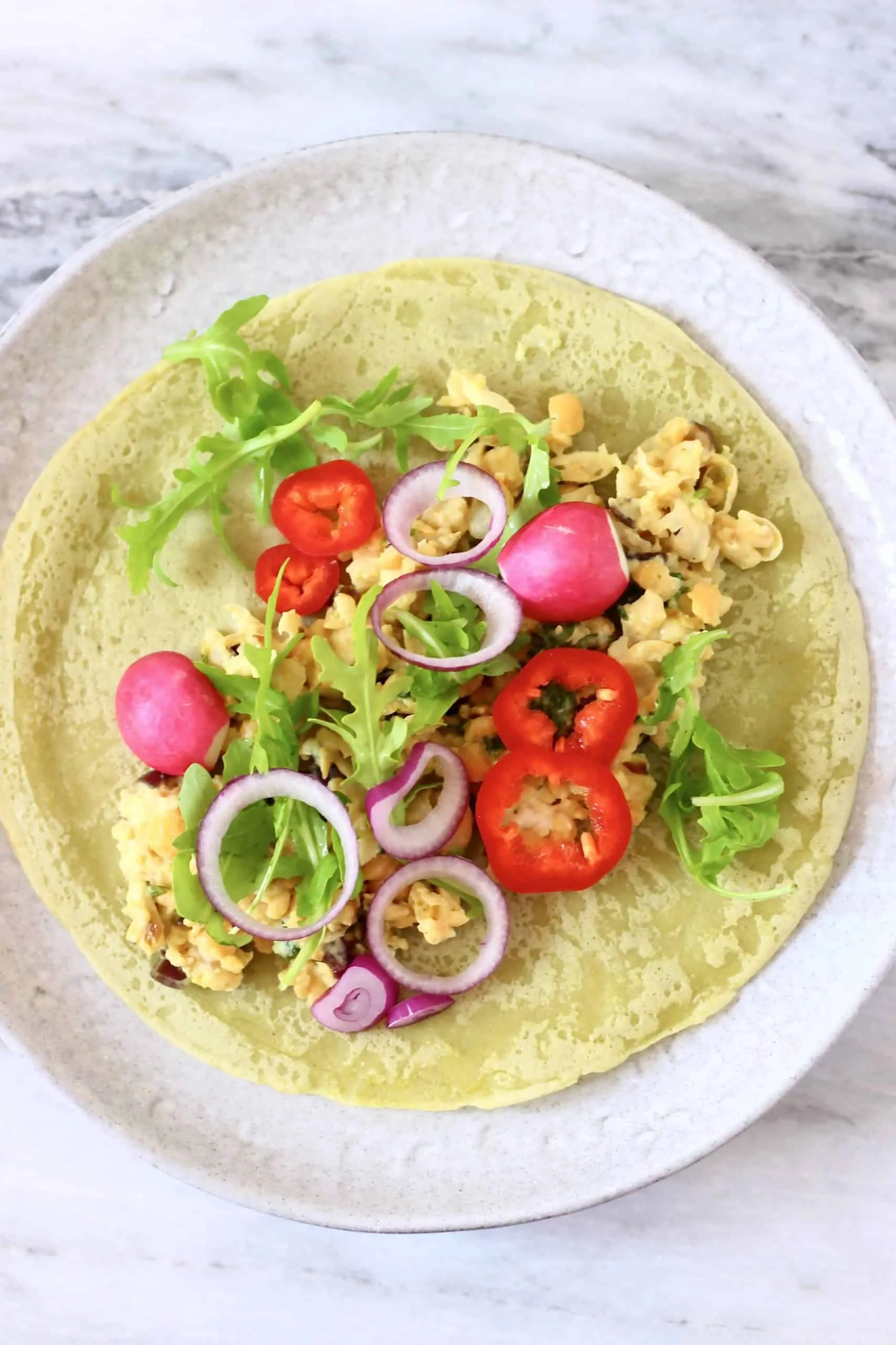 A green gluten-free vegan wrap topped with beans and salad on a white plate