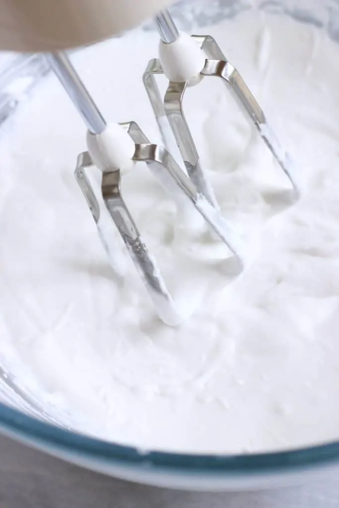 Vegan cream cheese frosting in a glass bowl with an electric whisk in it