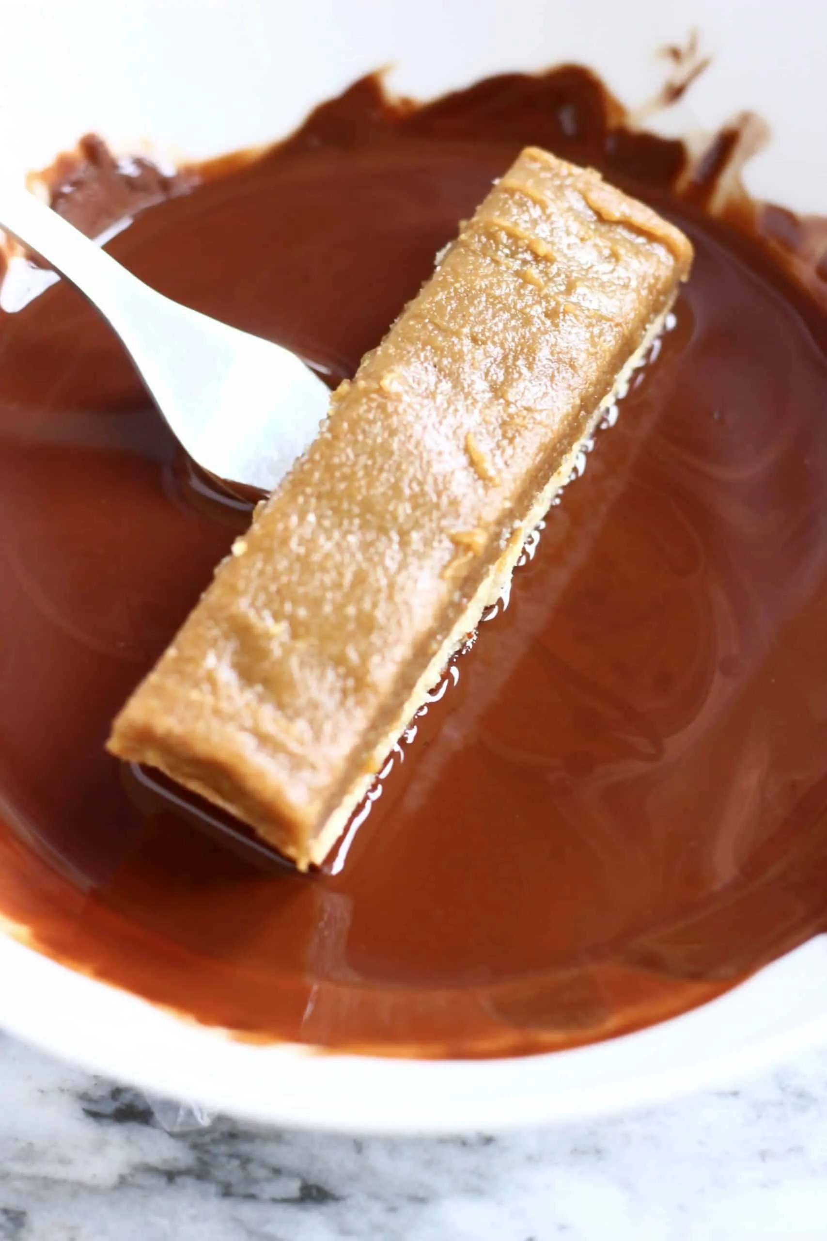 A vegan twix bar being dipped into a bowl of melted chocolate with a fork