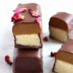 A vegan twix bar cut in half on top of a whole bar decorated with rose petals