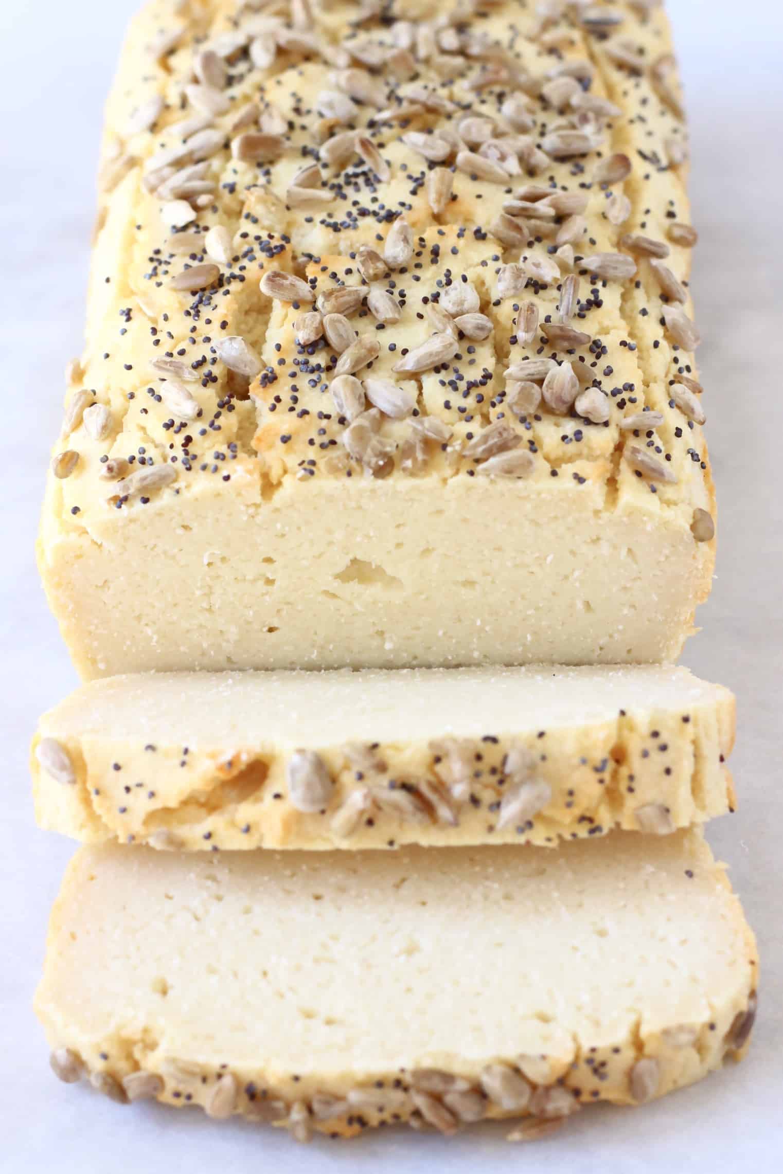 A loaf of coconut flour bread topped with seeds with two slices next to it