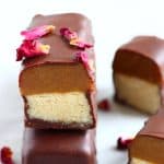 A vegan twix bar cut in half on top of a whole bar decorated with rose petals