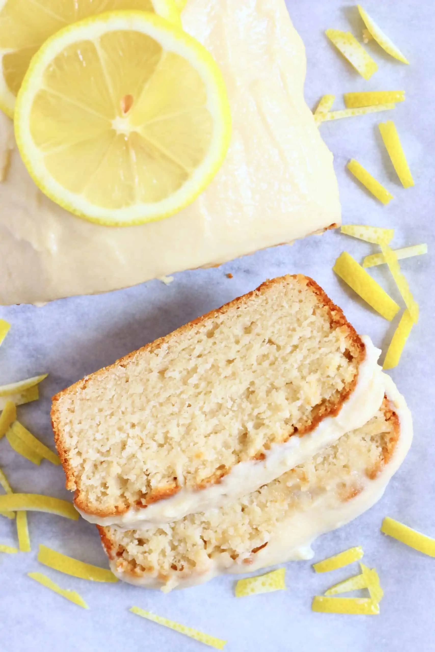A loaf of gluten-free vegan lemon bread topped with frosting with two slices next to it