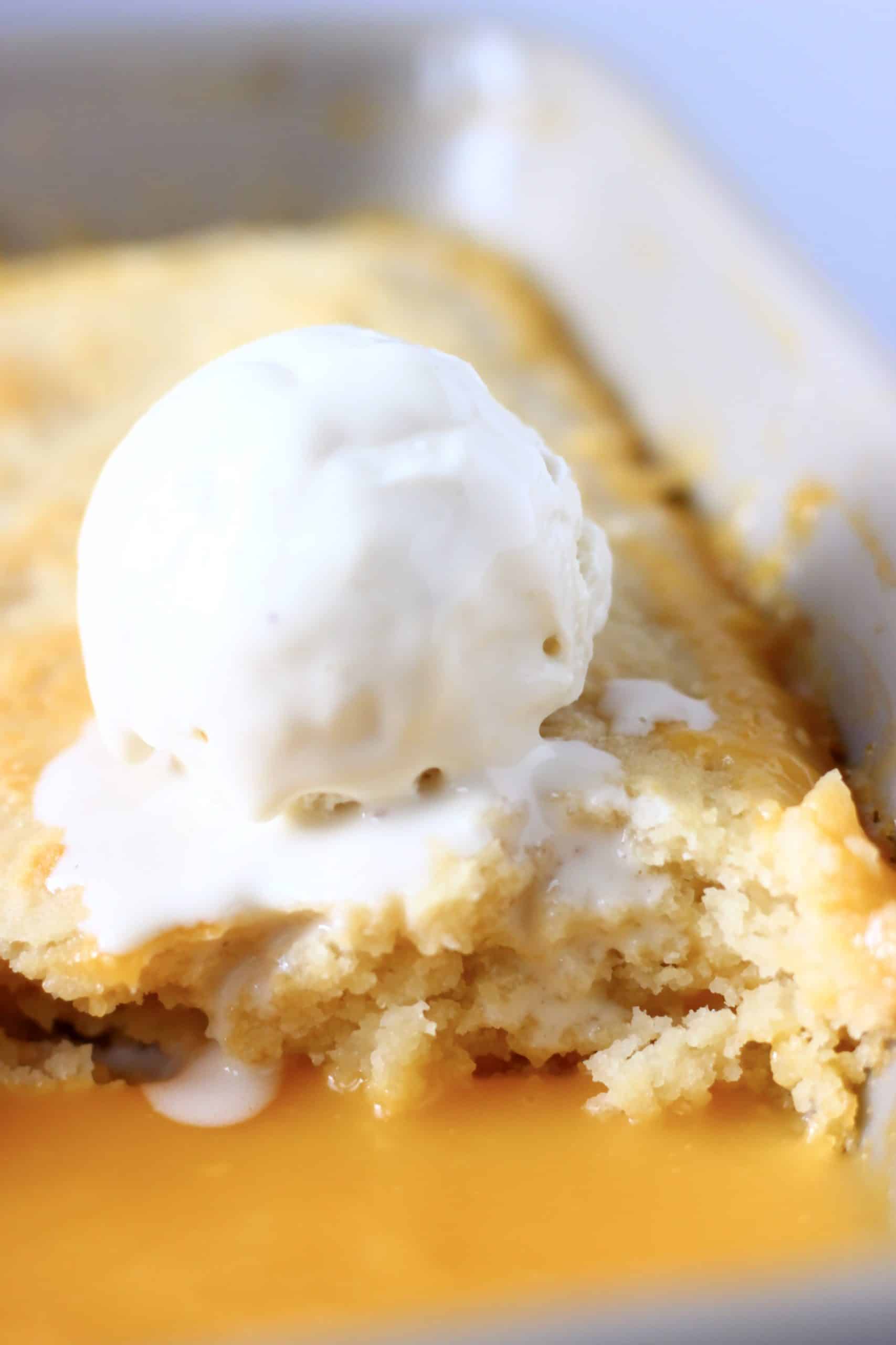 Vegan lemon pudding with lemon sauce topped with a scoop of vanilla ice cream in a rectangular baking dish