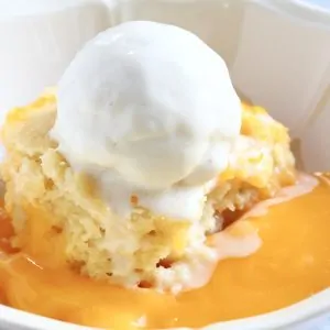 Vegan lemon pudding sponge in a bowl with lemon sauce and a scoop of vanilla ice cream on top