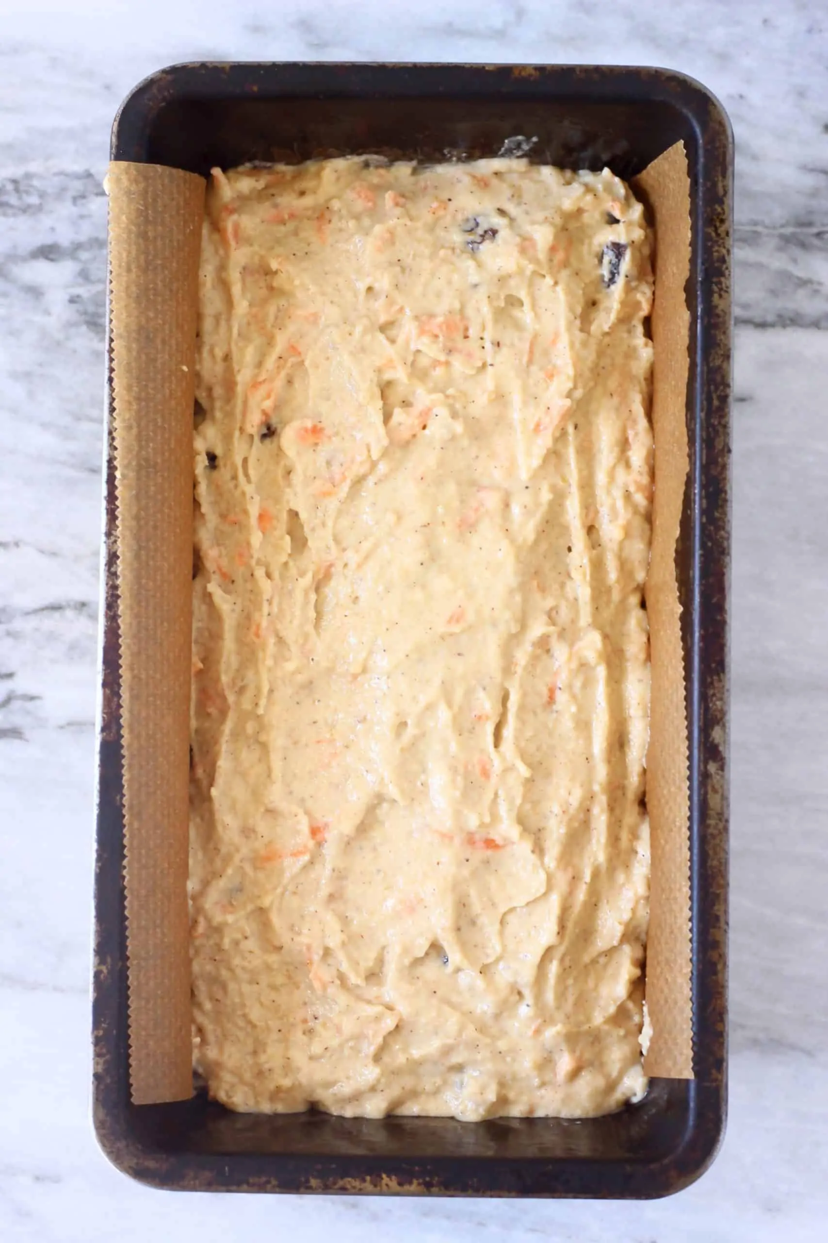 Vegan carrot bread batter in a loaf tin lined with baking paper
