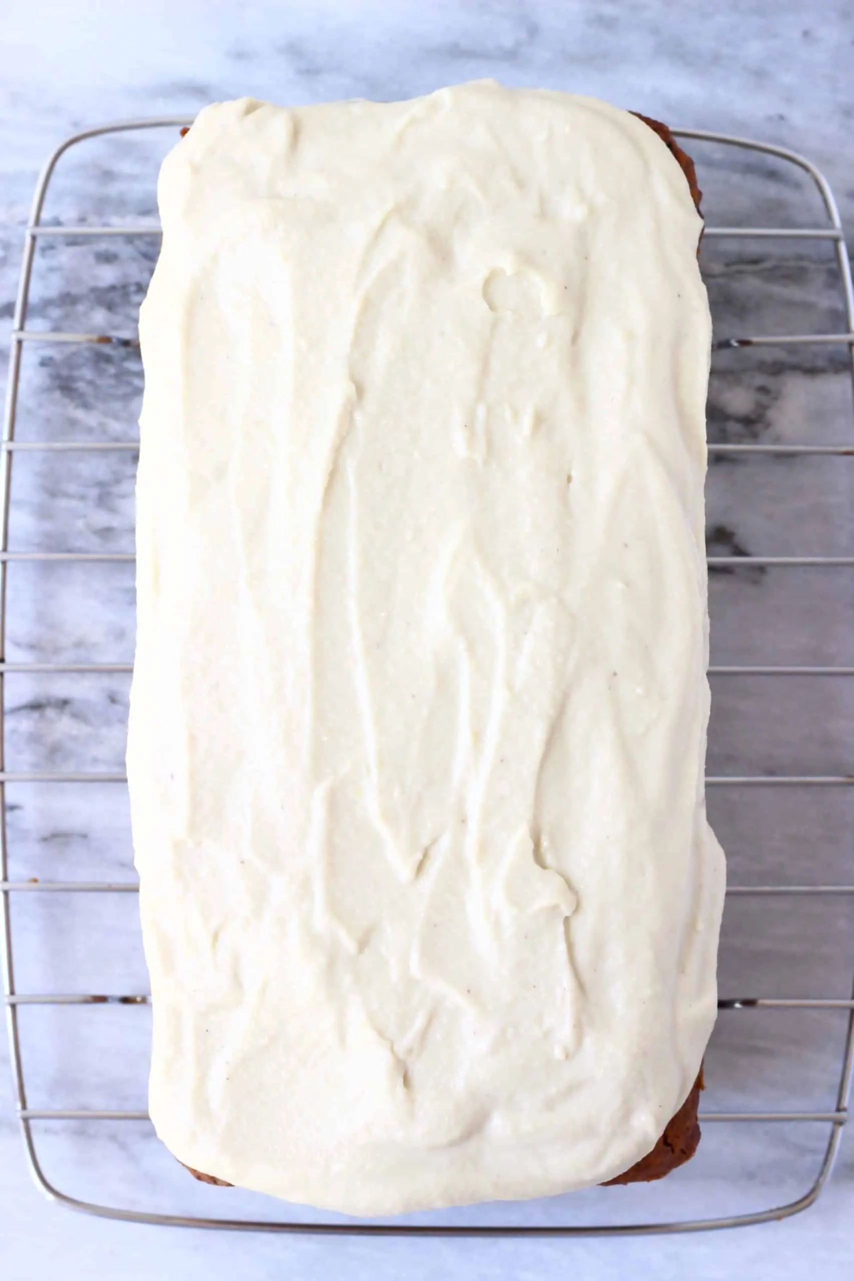 A loaf of vegan carrot bread topped with vegan cream cheese frosting on a wire rack