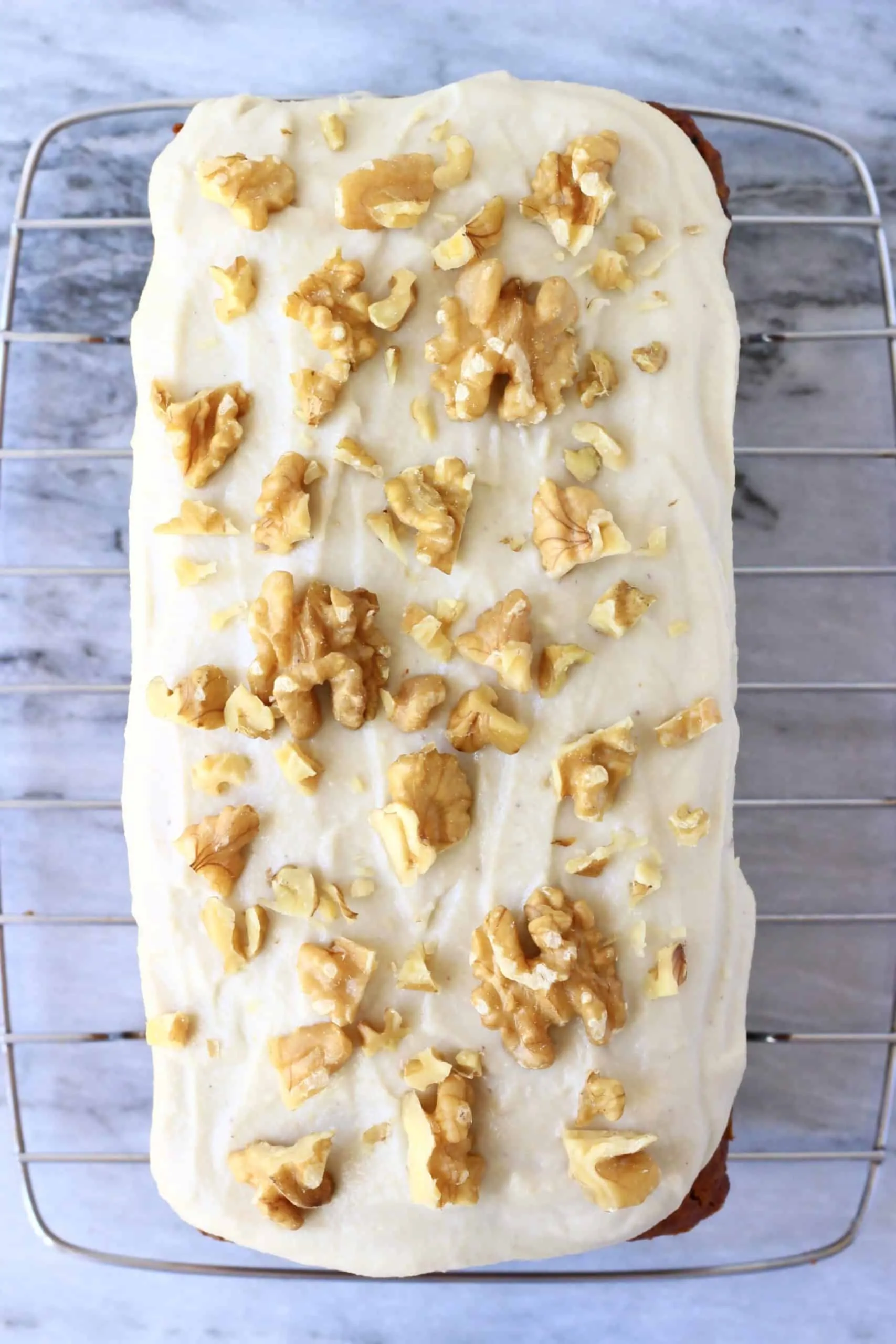 A loaf of vegan carrot bread topped with vegan cream cheese frosting and chopped walnuts on a wire rack