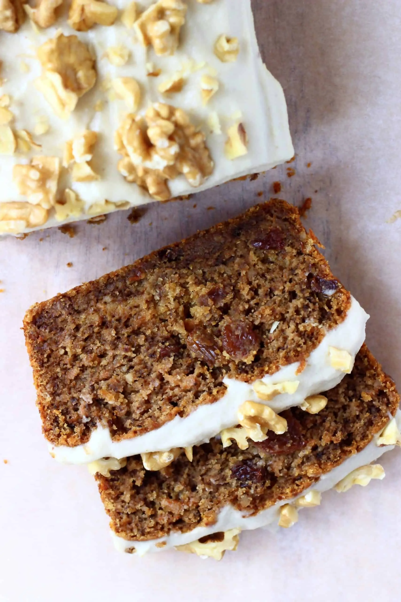 A loaf of vegan carrot bread topped with frosting and walnuts with two slices next to it