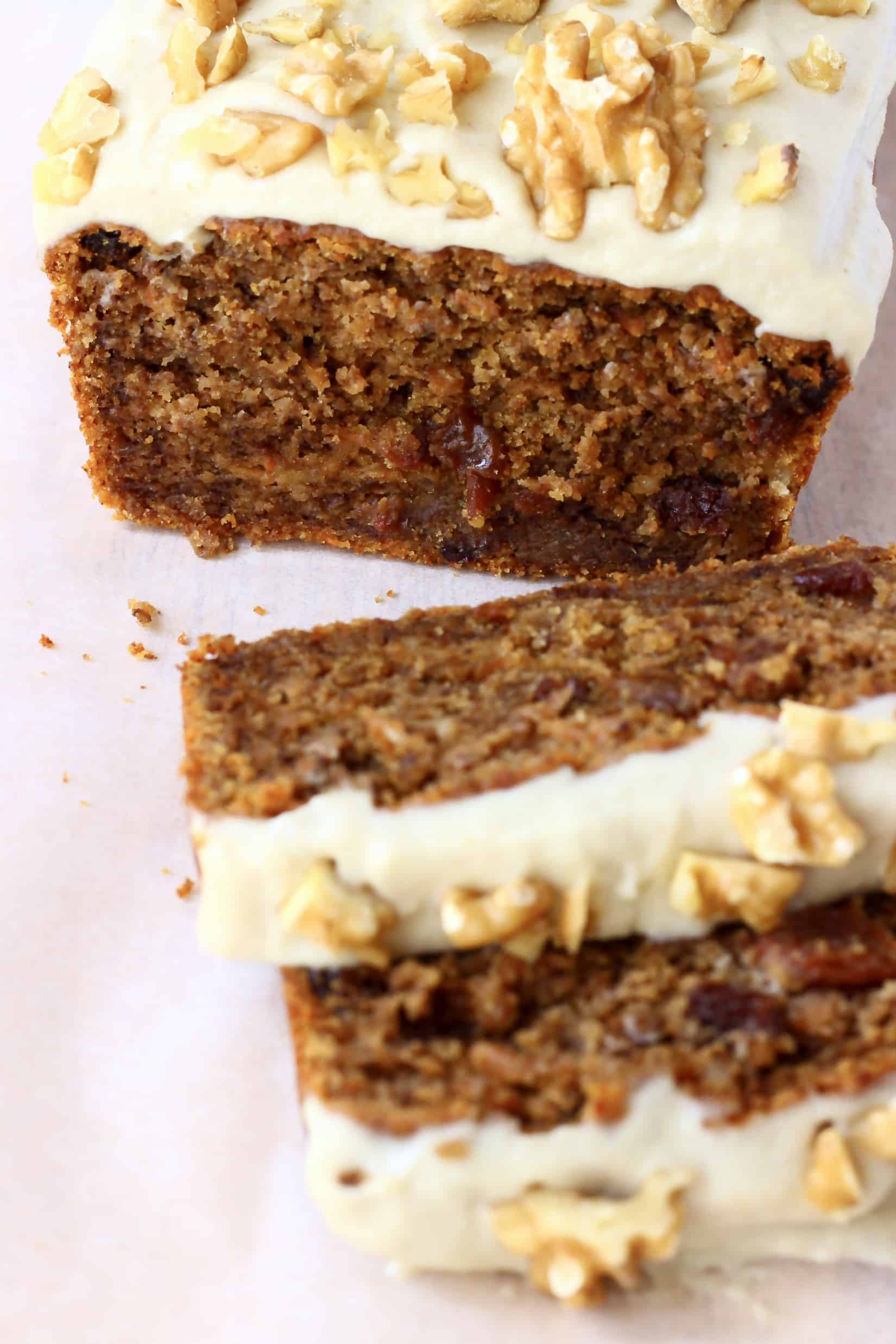 A loaf of vegan carrot bread topped with frosting and walnuts with two slices next to it