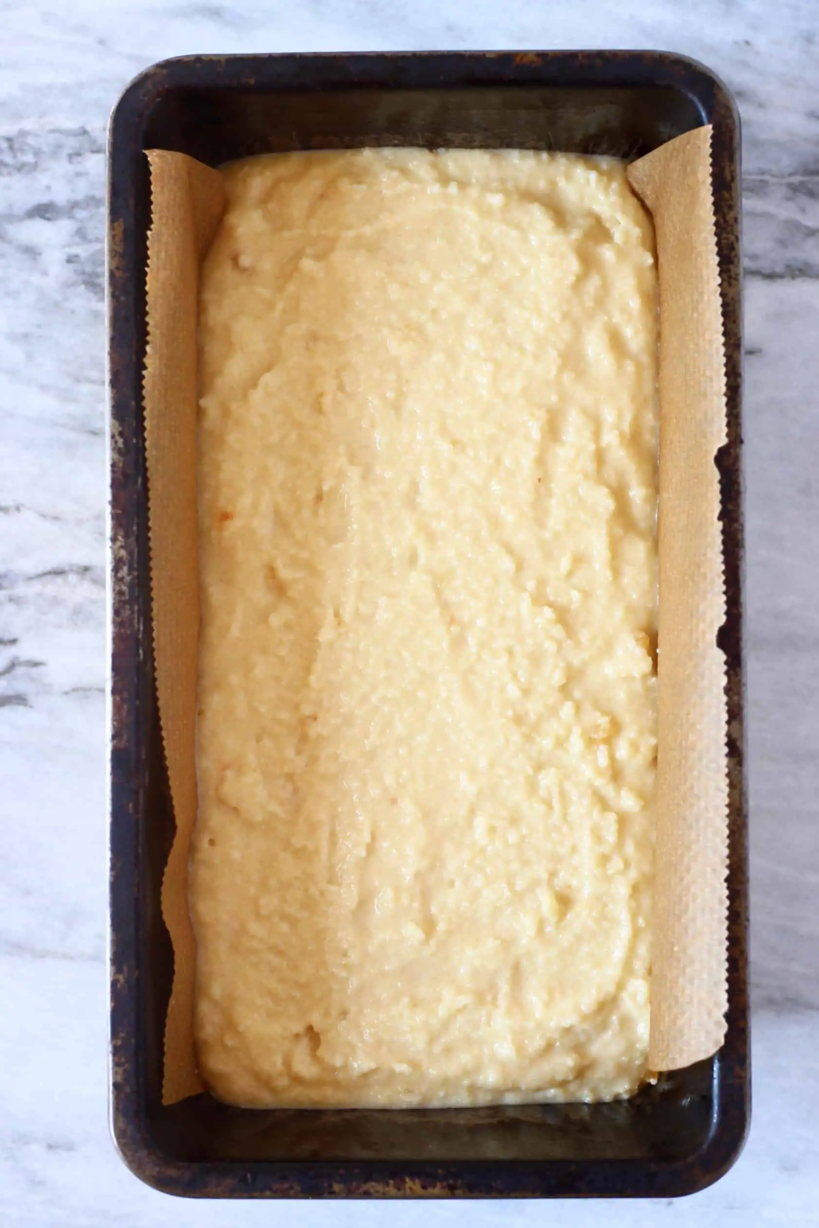 Raw vegan orange bread batter in a loaf tin lined with baking paper