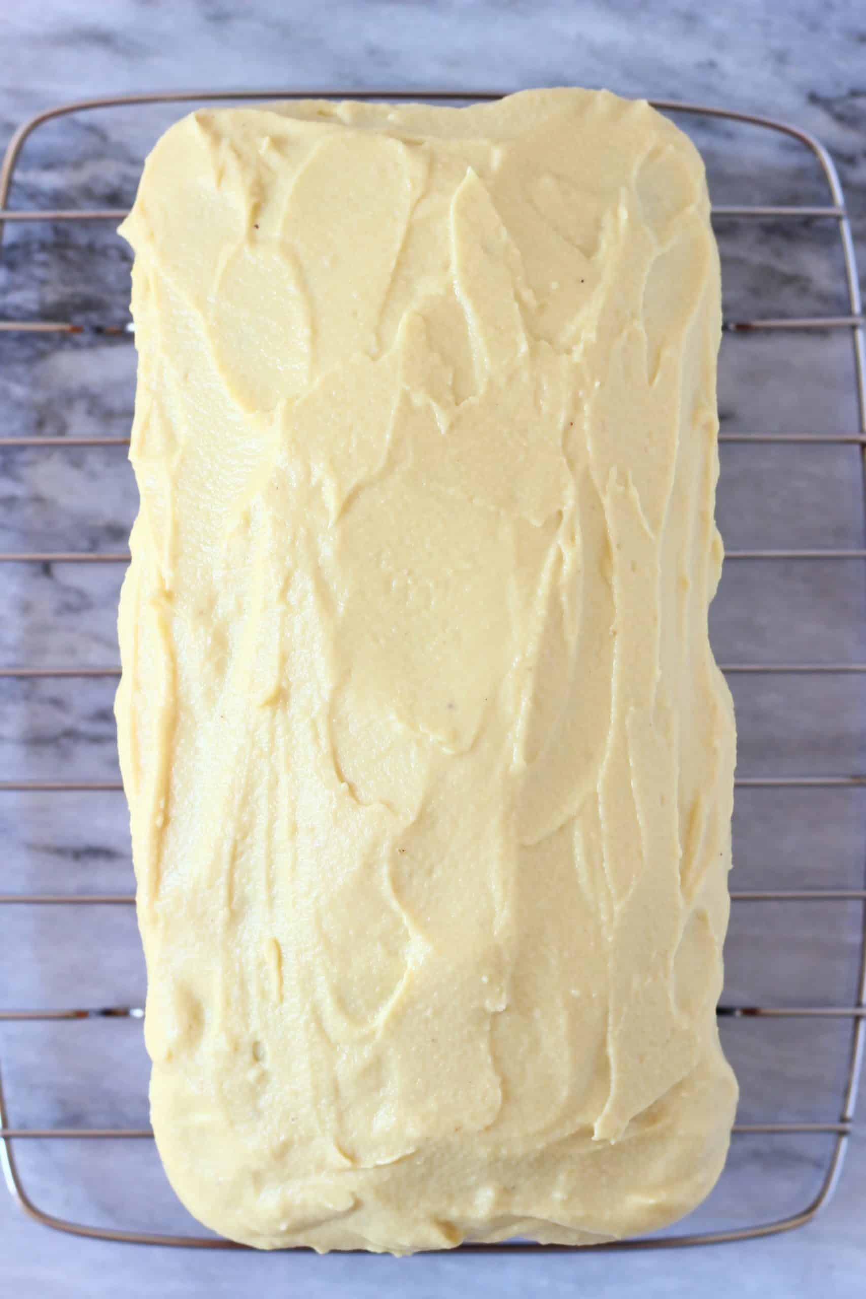 Vegan orange buttercream frosting spread over a loaf of vegan orange bread on a wire rack