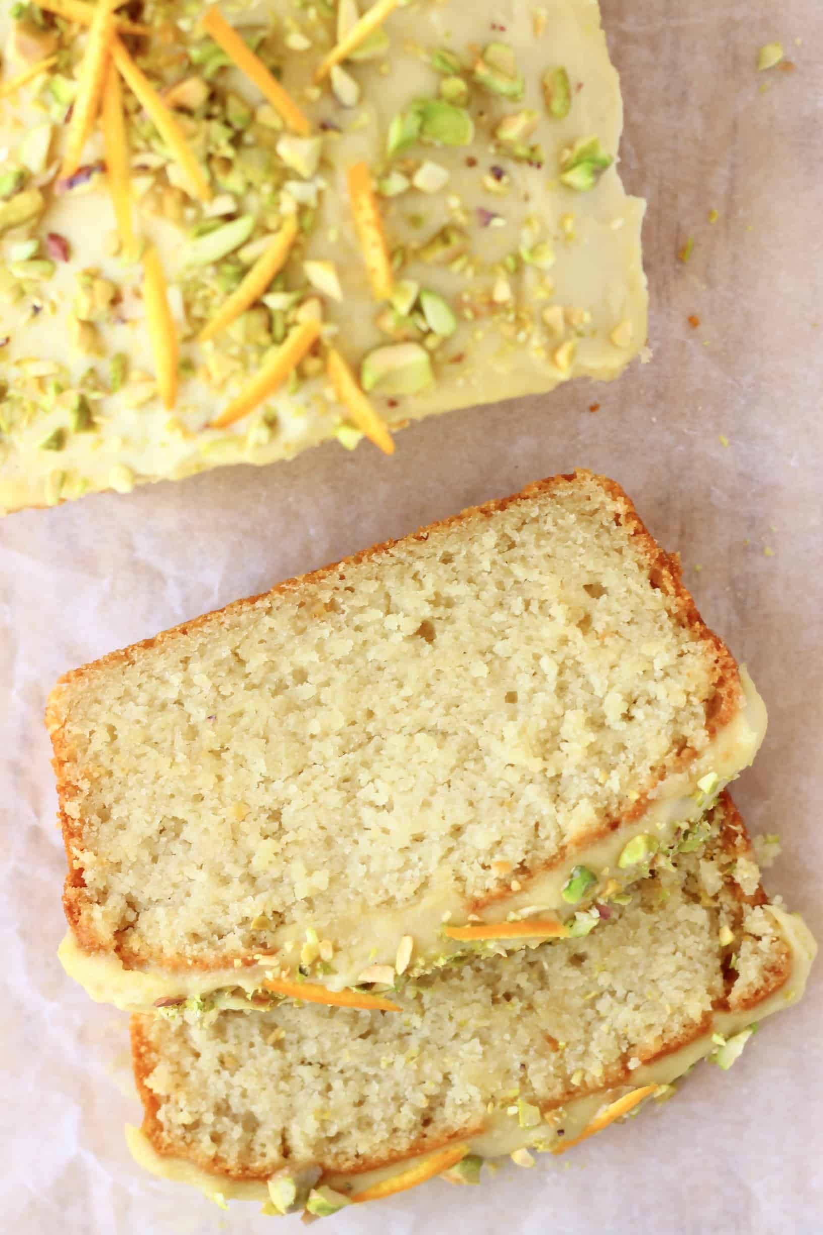 A loaf of vegan orange bread topped with frosting and chopped pistachios with two slices next to it