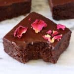 Three avocado brownies with chocolate frosting and rose petals with a bite taken out of one