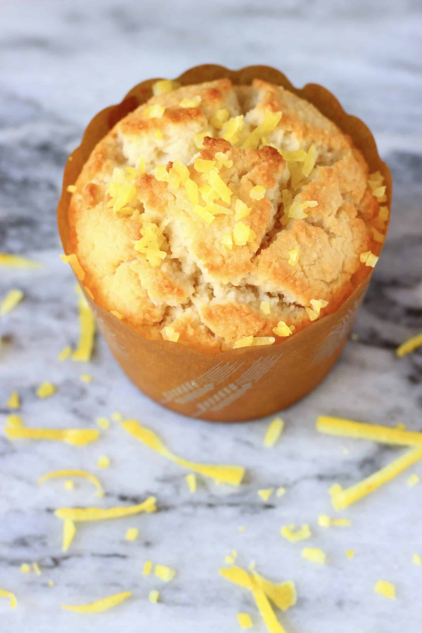 A gluten-free vegan lemon muffin in a brown muffin case topped with lemon zest