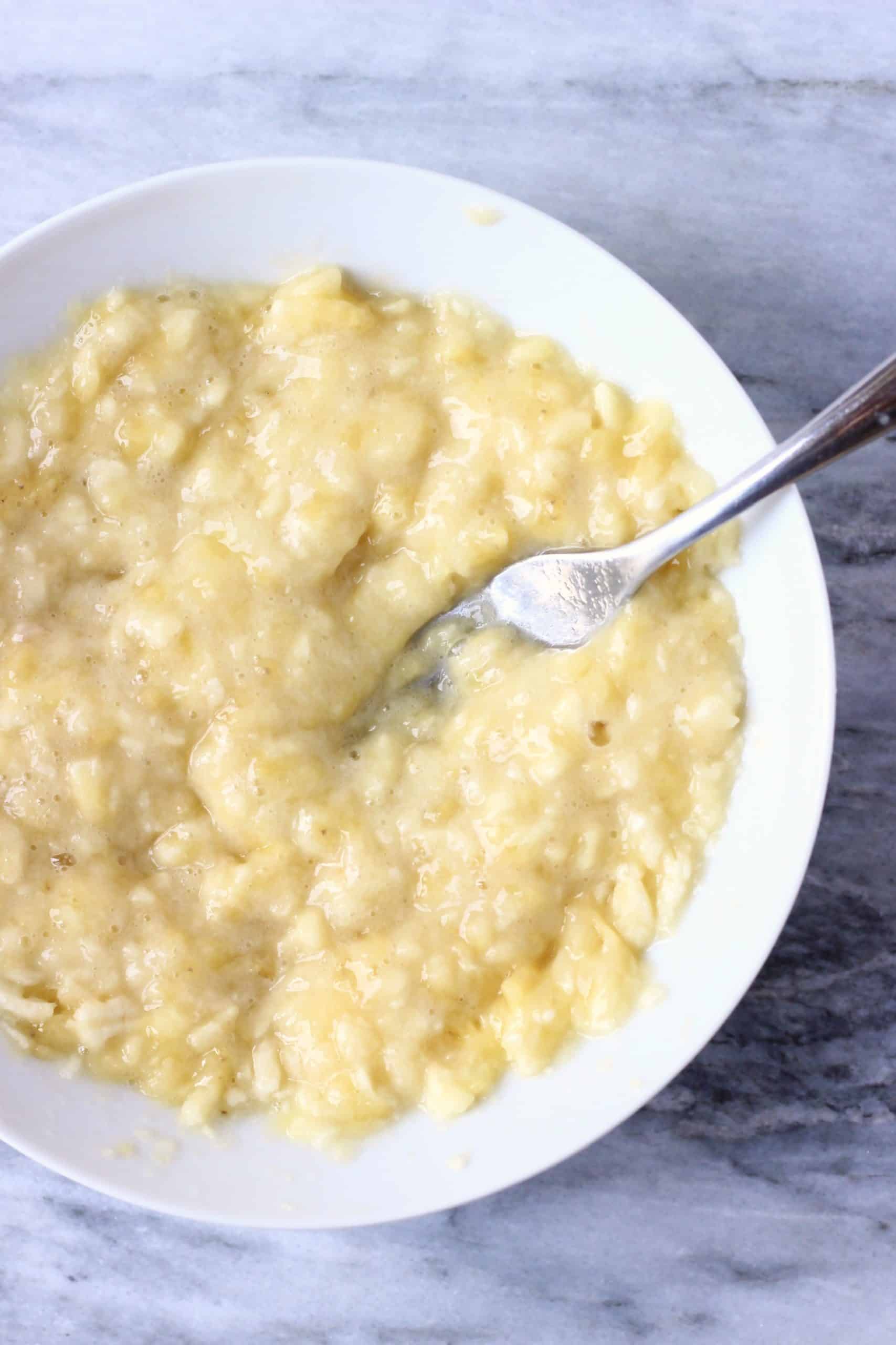 Mashed bananas in a white bowl with a fork