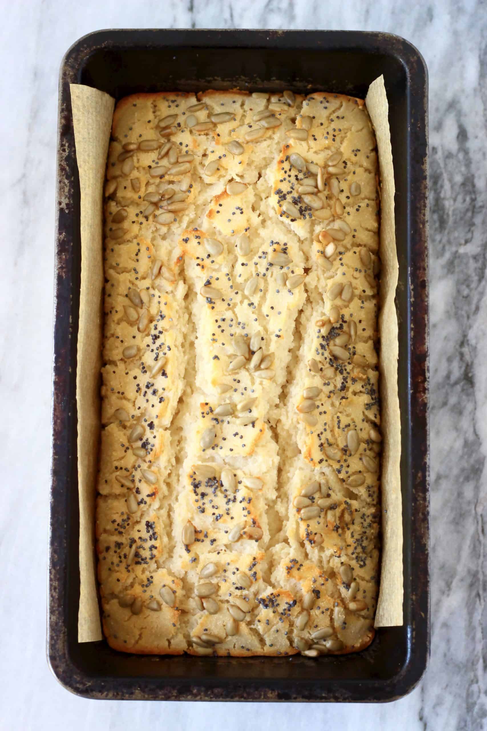 A loaf of coconut flour bread topped with sunflower seeds and poppy seeds in a loaf tin lined with baking paper