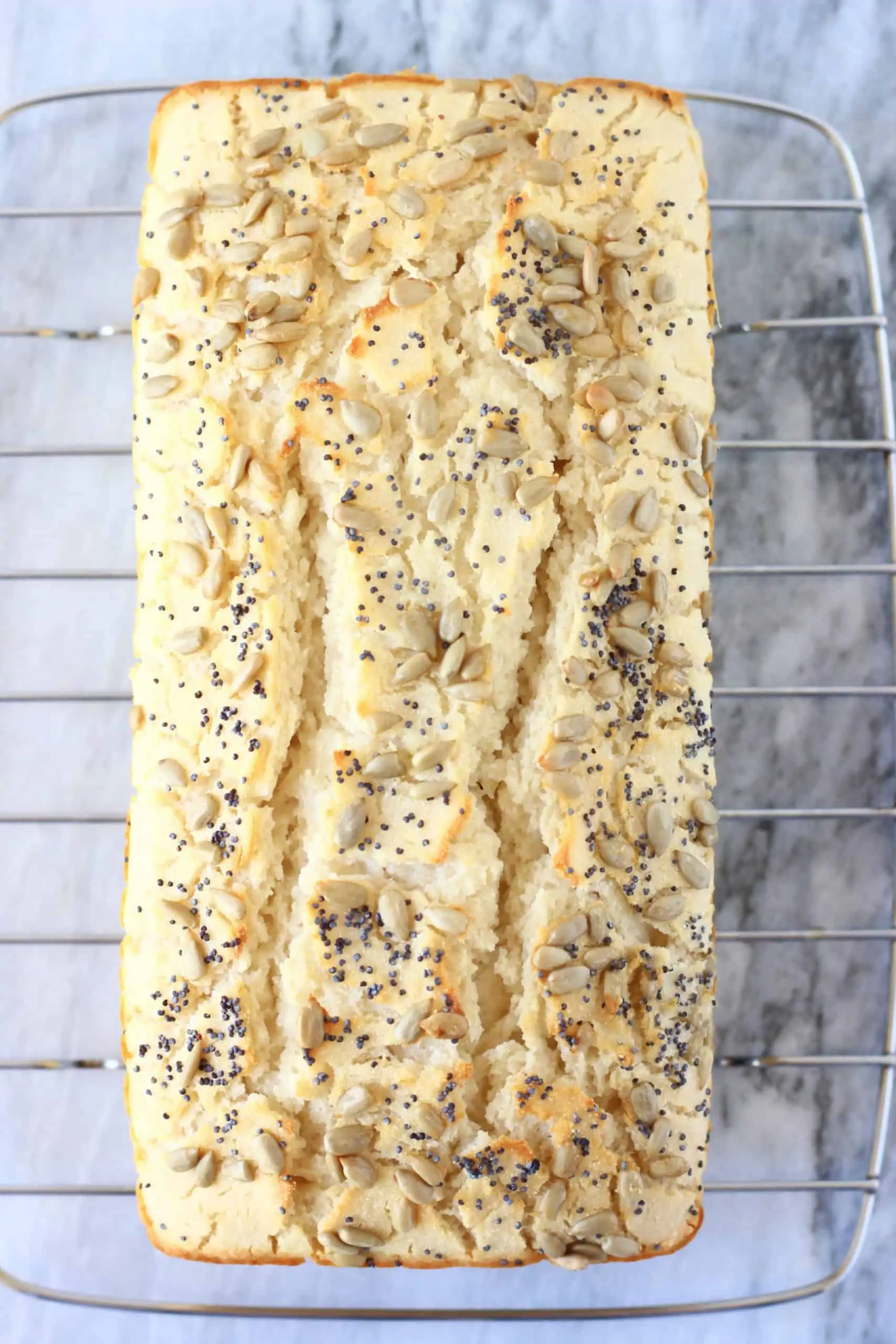 A loaf of coconut flour bread topped with sunflower seeds and poppy seeds on a wire rack