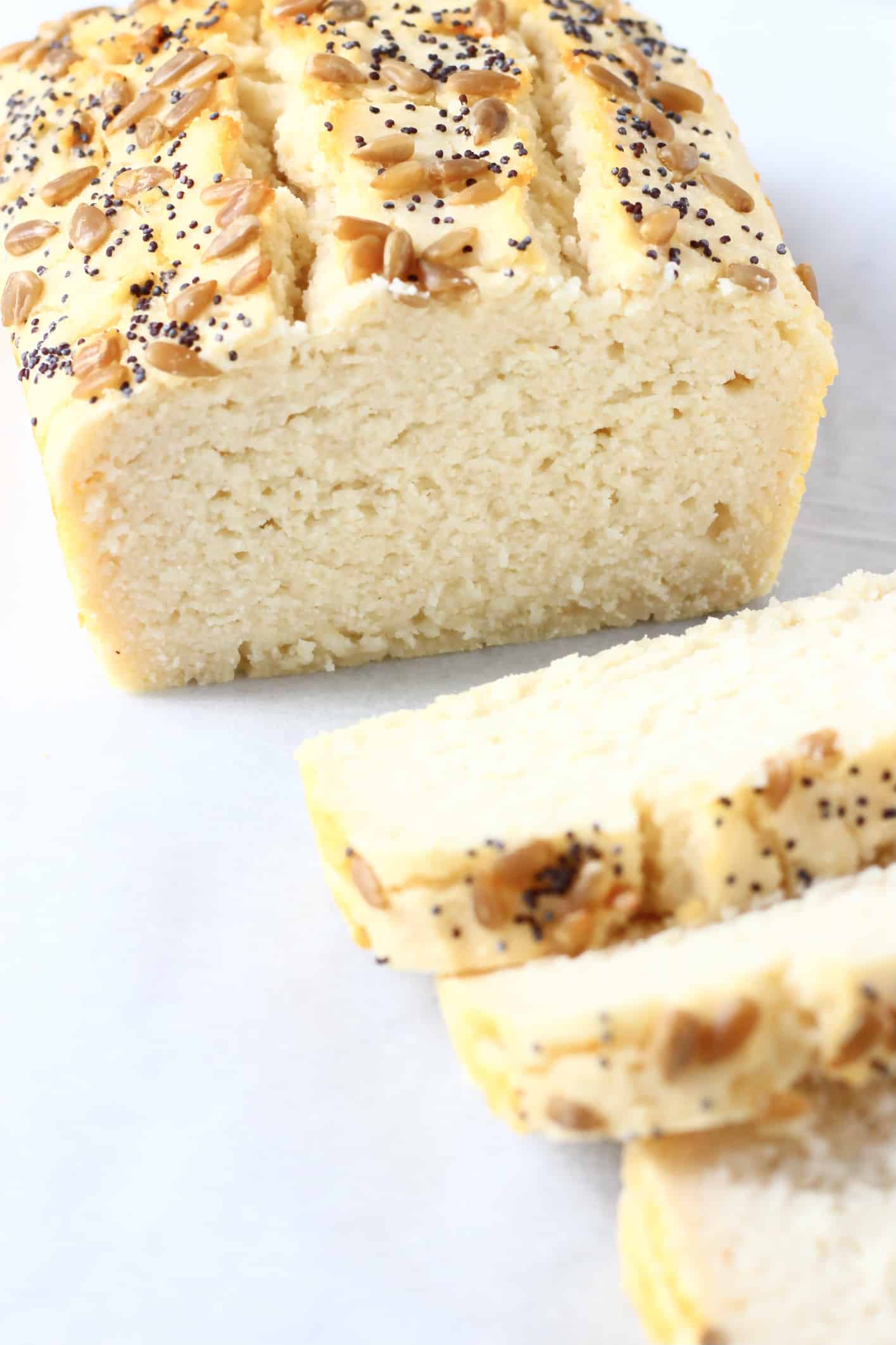 A loaf of coconut flour bread topped with sunflower seeds and poppy seeds with three slices next to it