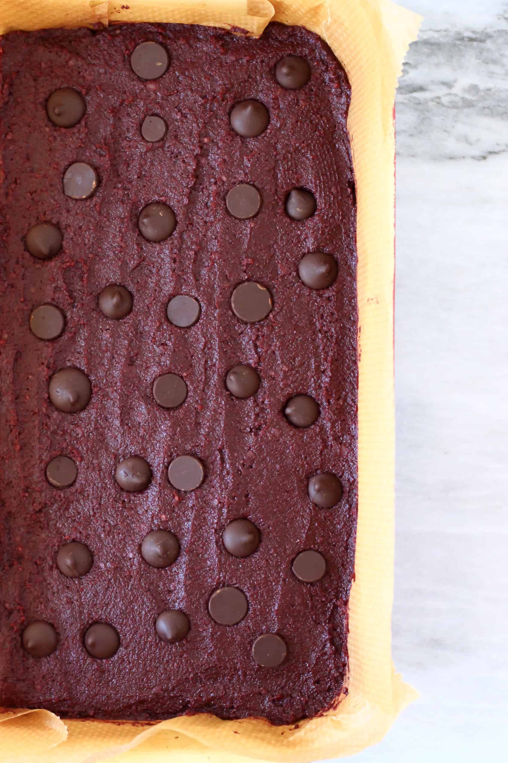 Beetroot brownie batter with chocolate chips in a square baking tin lined with baking paper