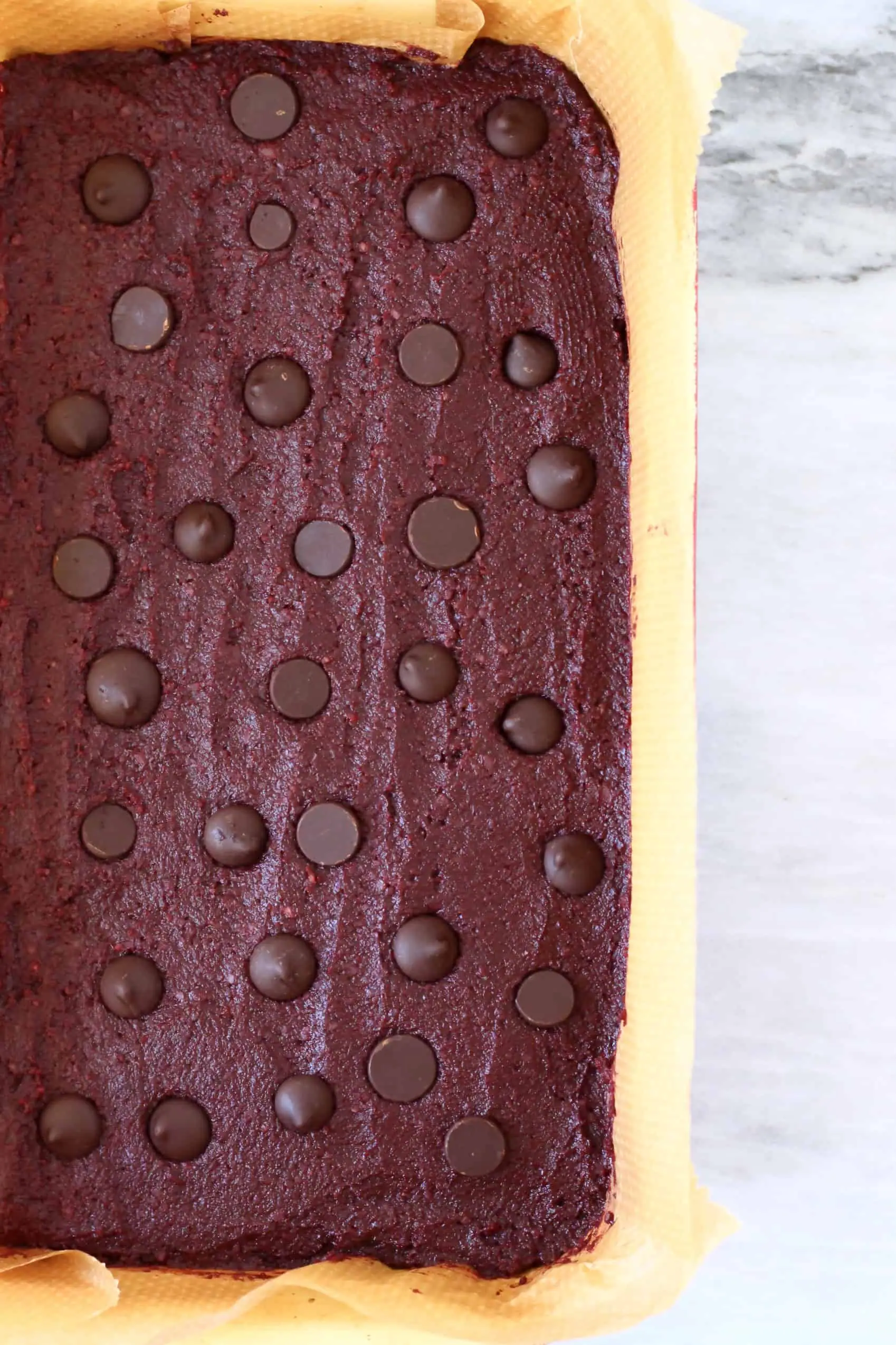 Beetroot brownie batter with chocolate chips in a square baking tin lined with baking paper