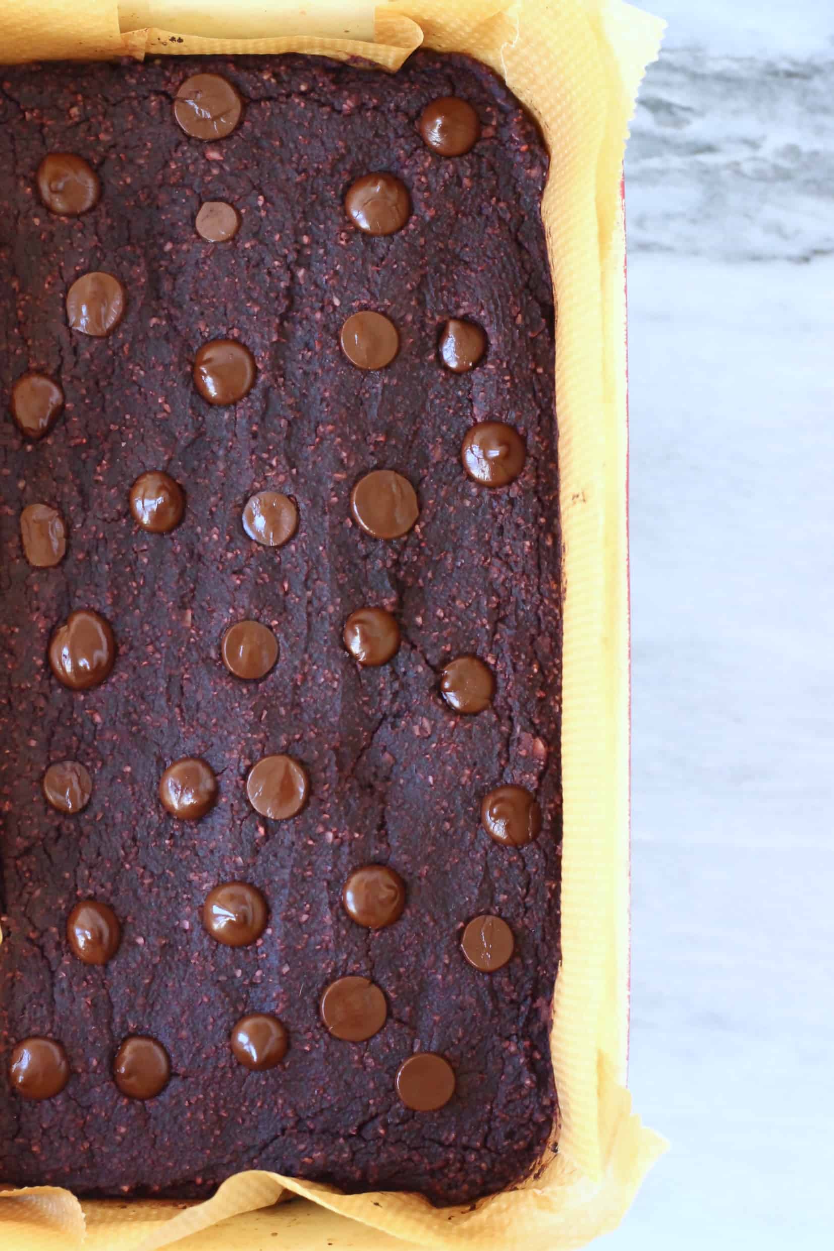 Cooked beetroot brownies with chocolate chips in a square baking tin lined with baking paper