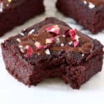 Three beetroot brownies with chocolate frosting, rose petals and salt flakes with a bite taken out of one