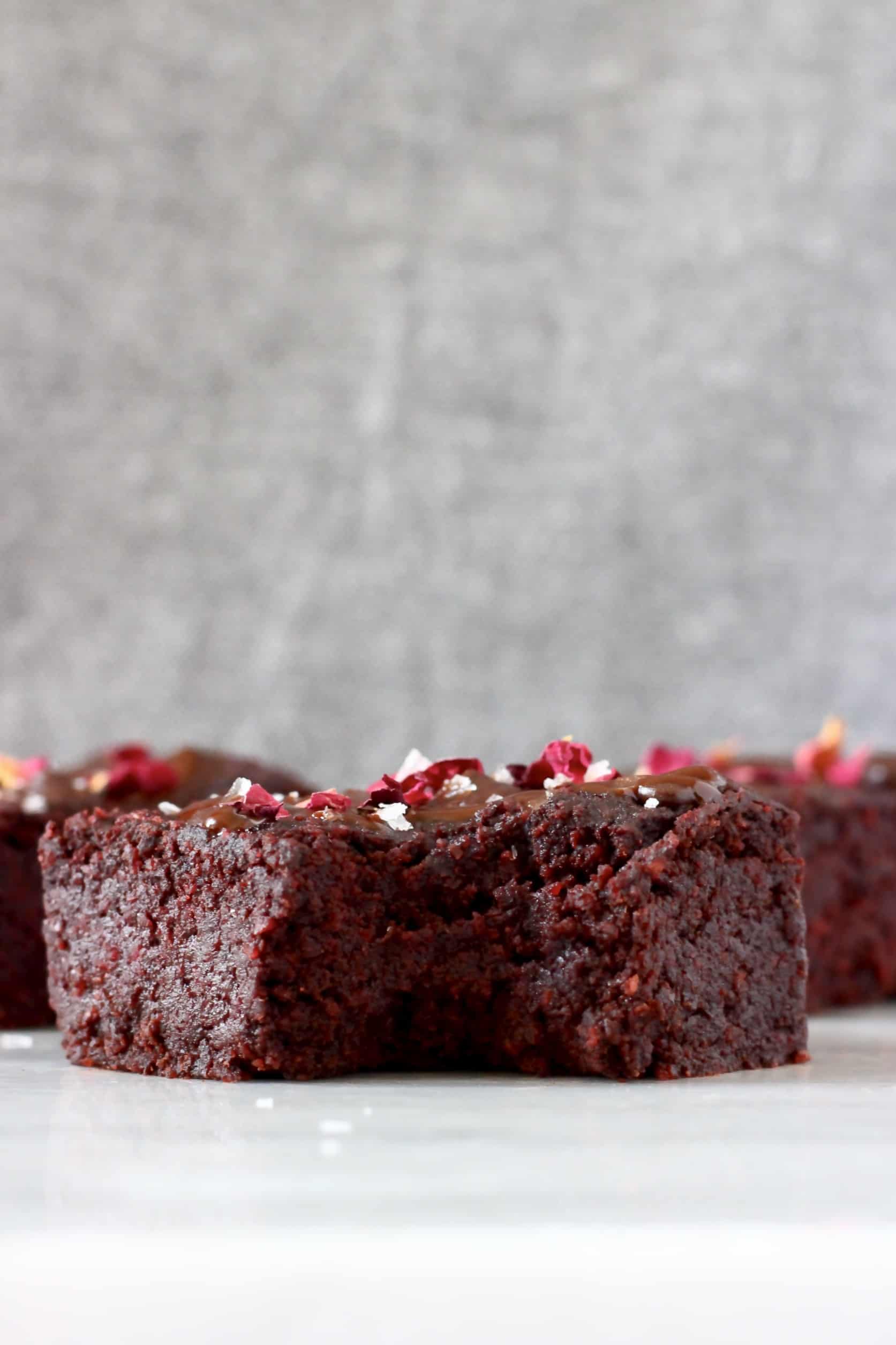 Three beetroot brownies with chocolate frosting and rose petals with a bite taken out of one