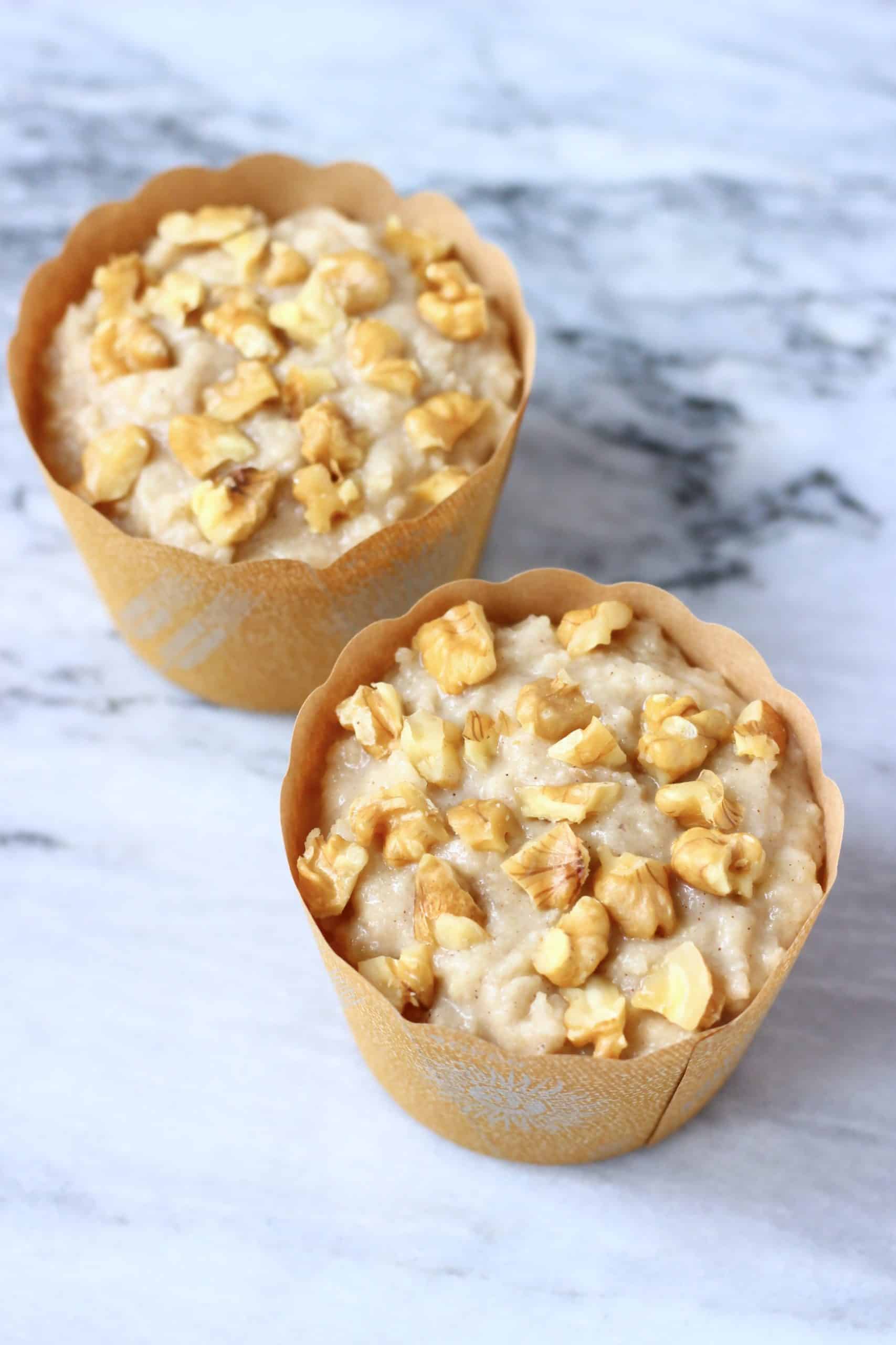 Raw gluten-free vegan banana muffin batter in two brown muffin cases topped with chopped walnuts