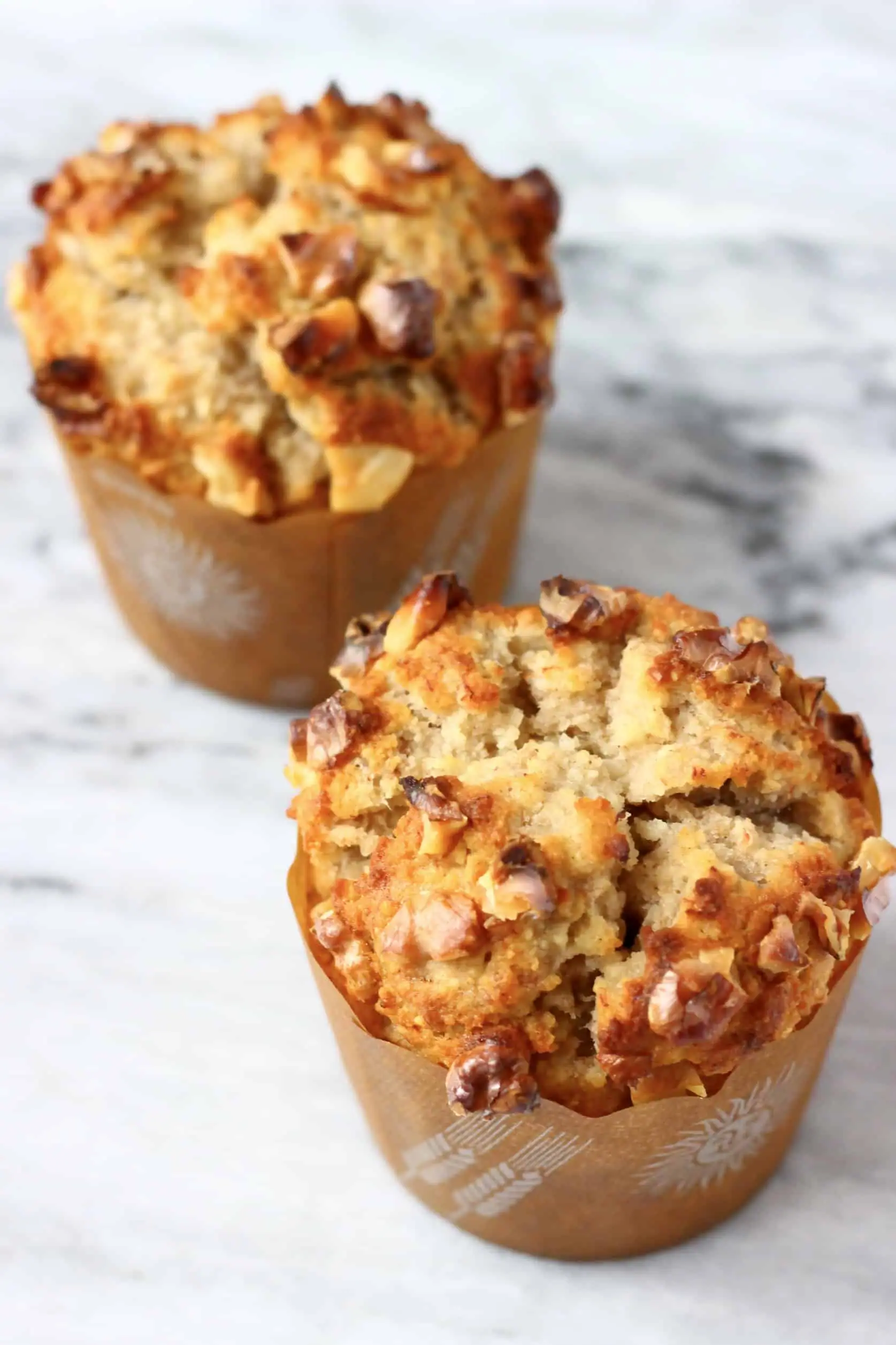 Two gluten-free vegan banana muffins topped with chopped walnuts in brown muffin cases