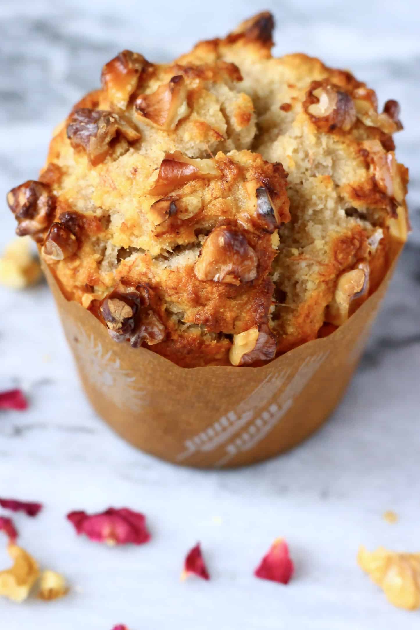 A gluten-free vegan banana muffin topped with chopped walnuts in a brown muffin case