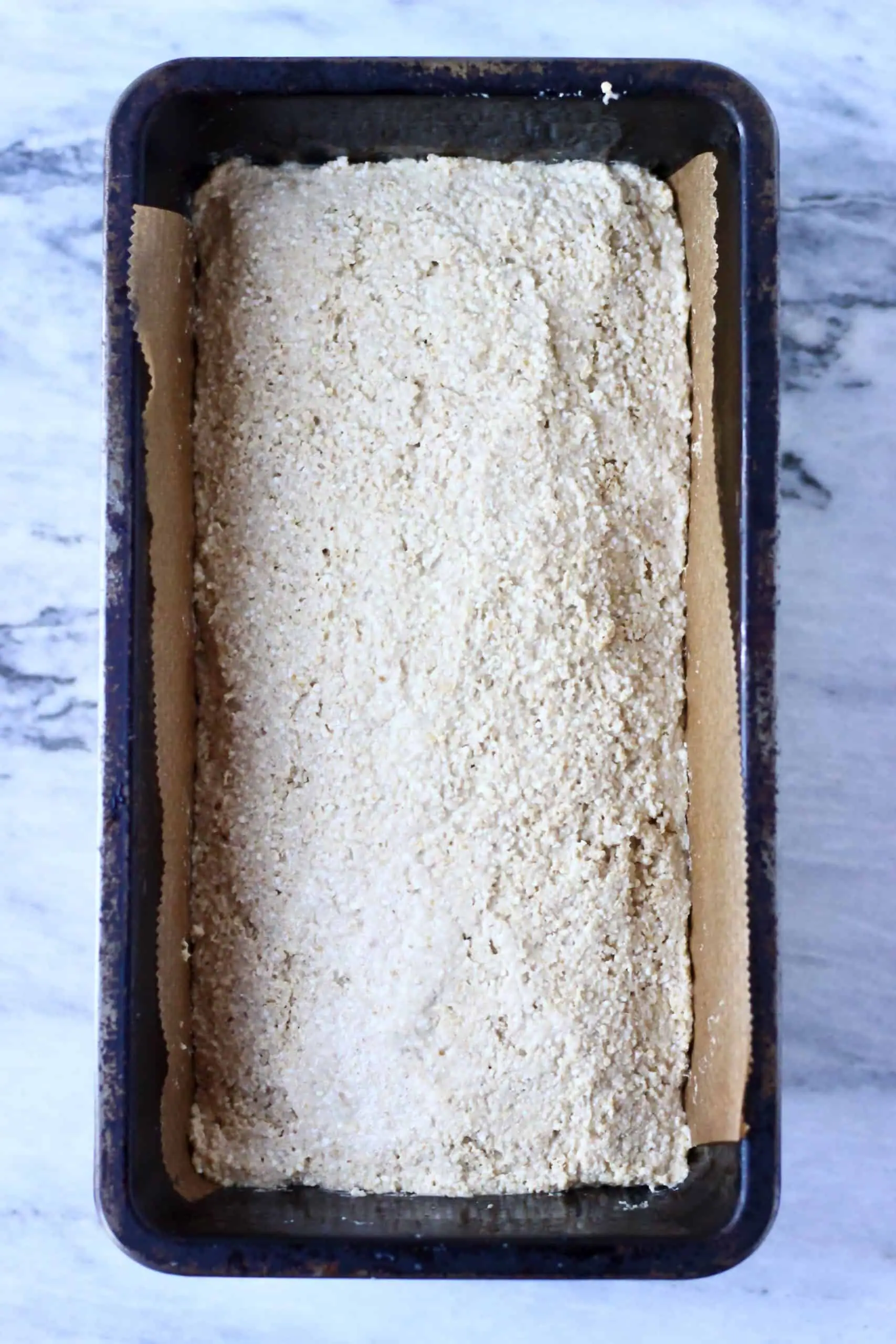 Quinoa bread batter in a loaf tin lined with baking paper