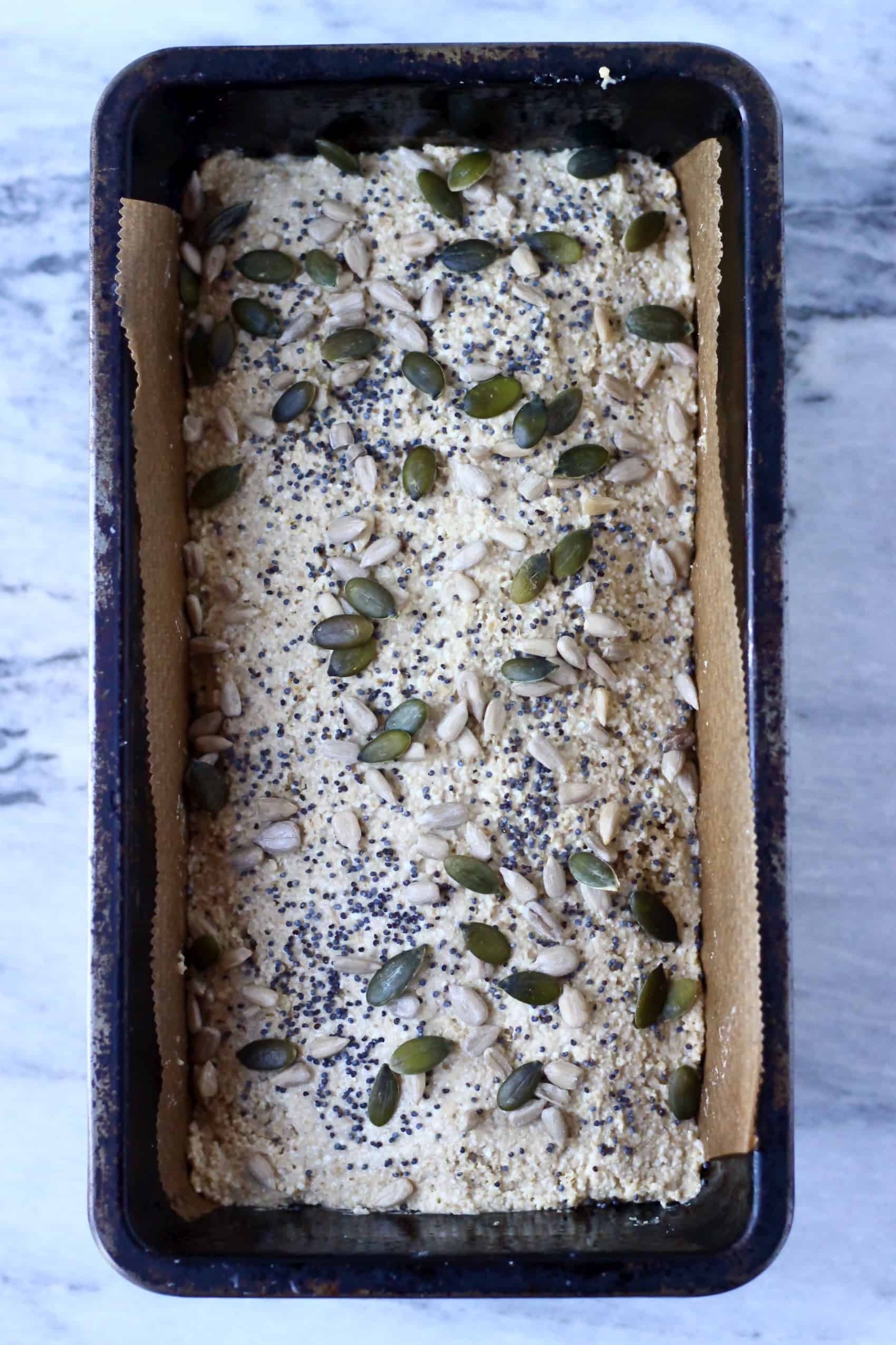 Quinoa bread batter in a loaf tin sprinkled with mixed seeds