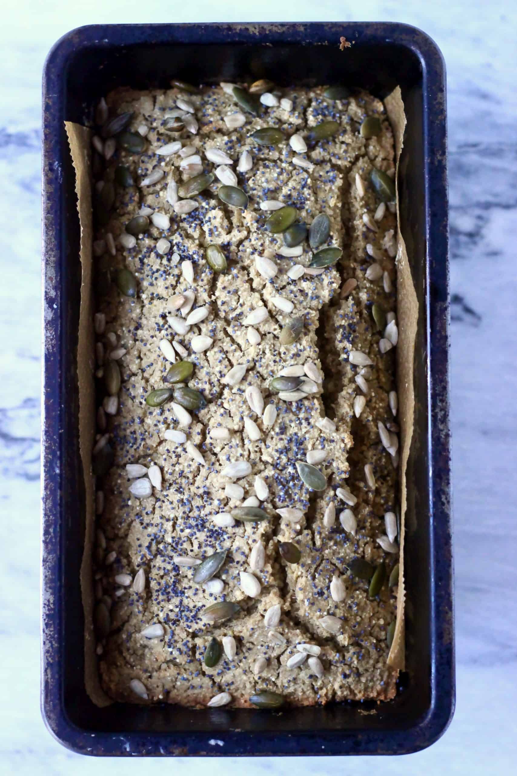 Quinoa bread topped with mixed seeds in a loaf tin lined with baking paper