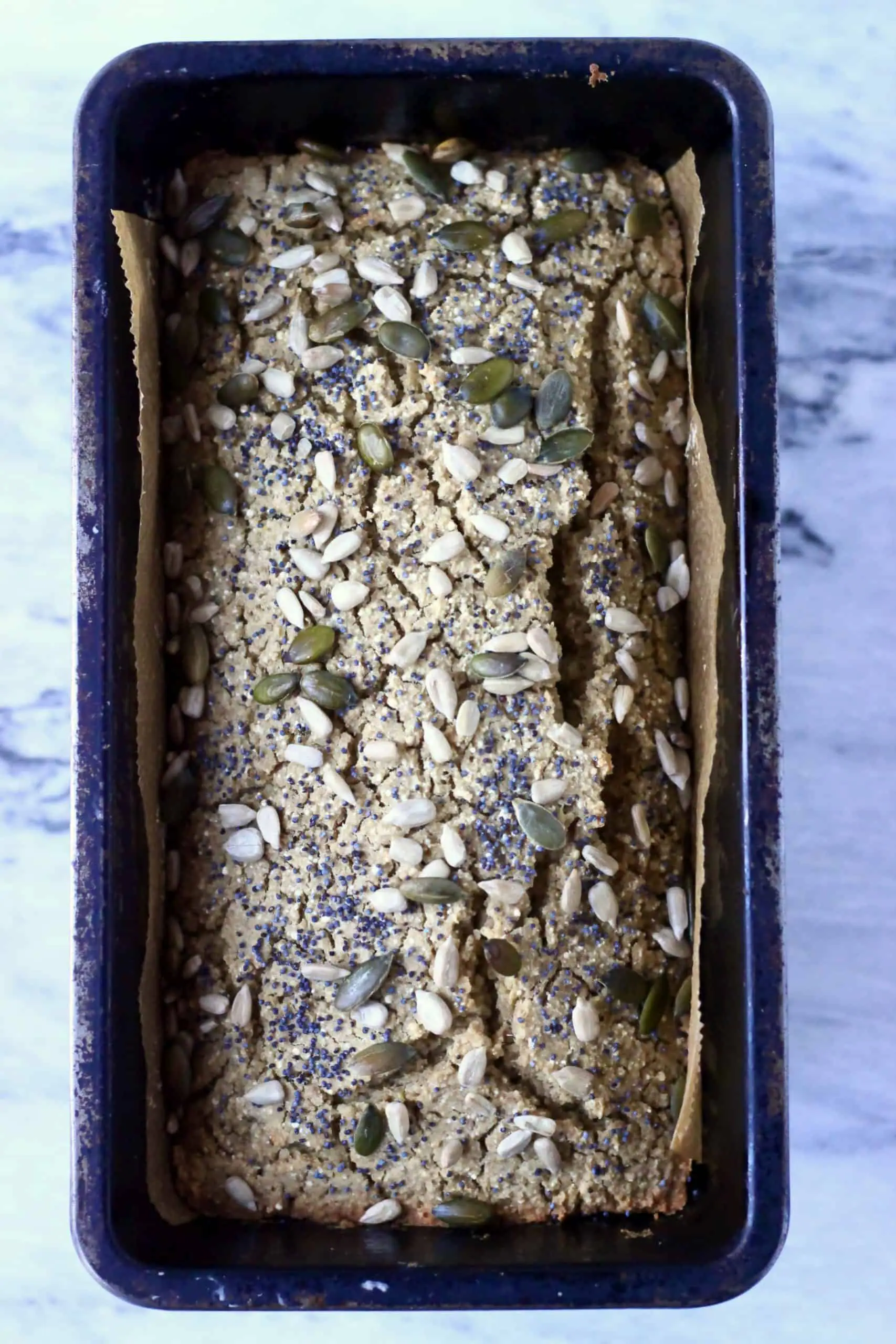 Quinoa bread topped with mixed seeds in a loaf tin lined with baking paper