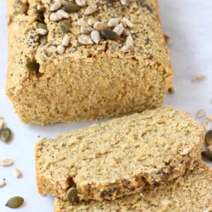 A loaf of quinoa bread topped with seeds with two slices next to it