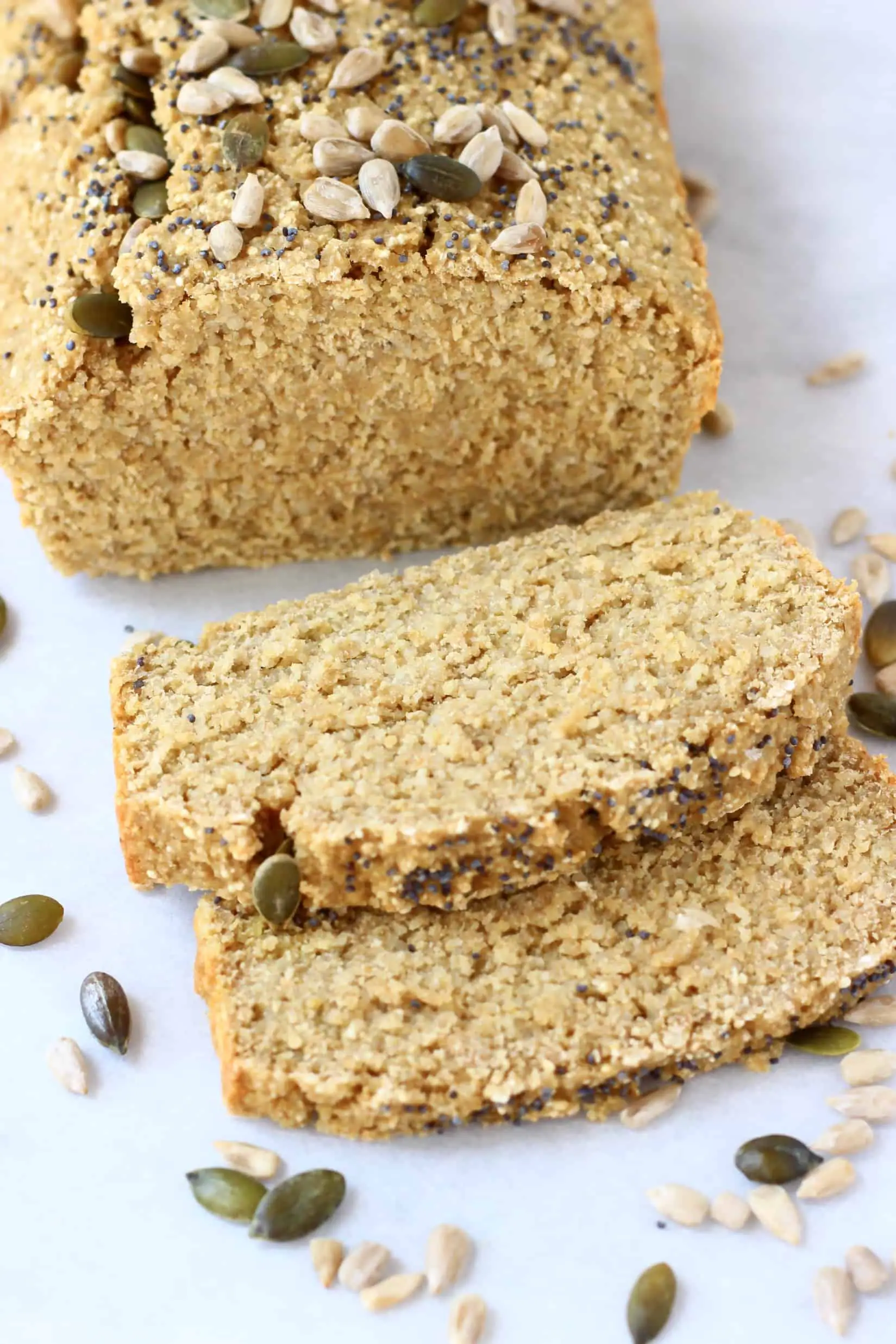 A loaf of quinoa bread topped with seeds with two slices next to it